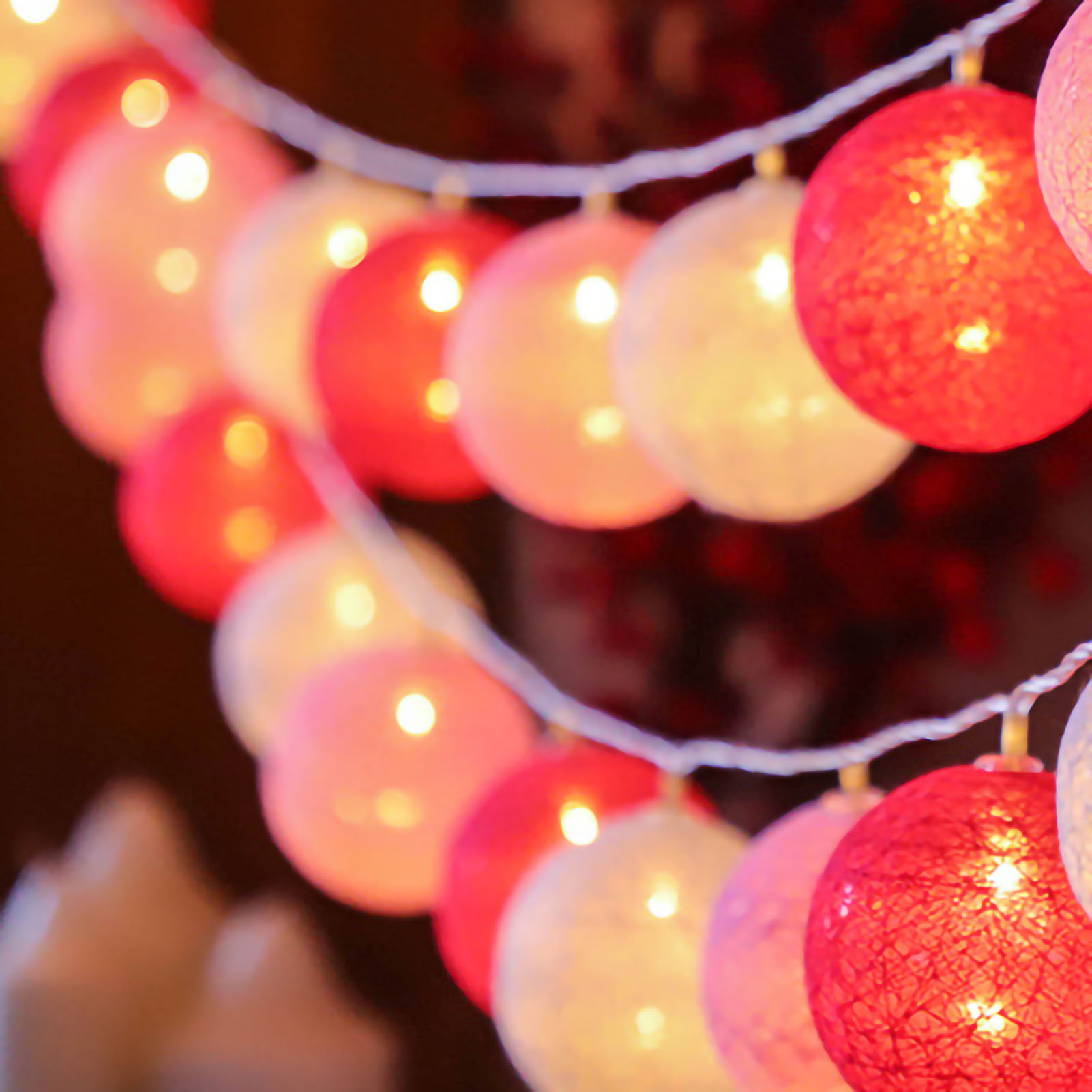 Lichterketten mit rot, rosa und weißen leuchtenden Kugeln. Der Hintergrund ist unscharf mit dunklem Ton.