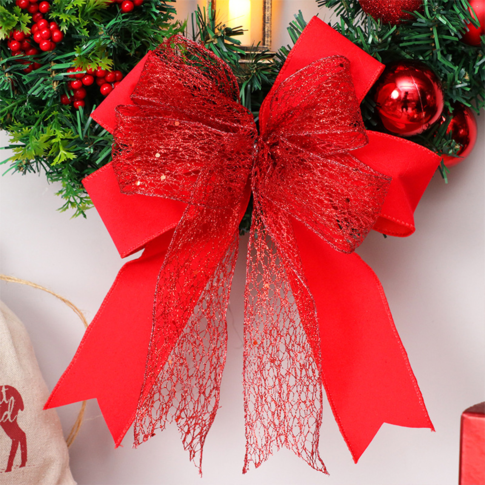 Ein Weihnachtskranz mit einer großen roten Schleife. Rote Ornamente und rote Beeren sind sichtbar. Links ist eine beige Tasche.