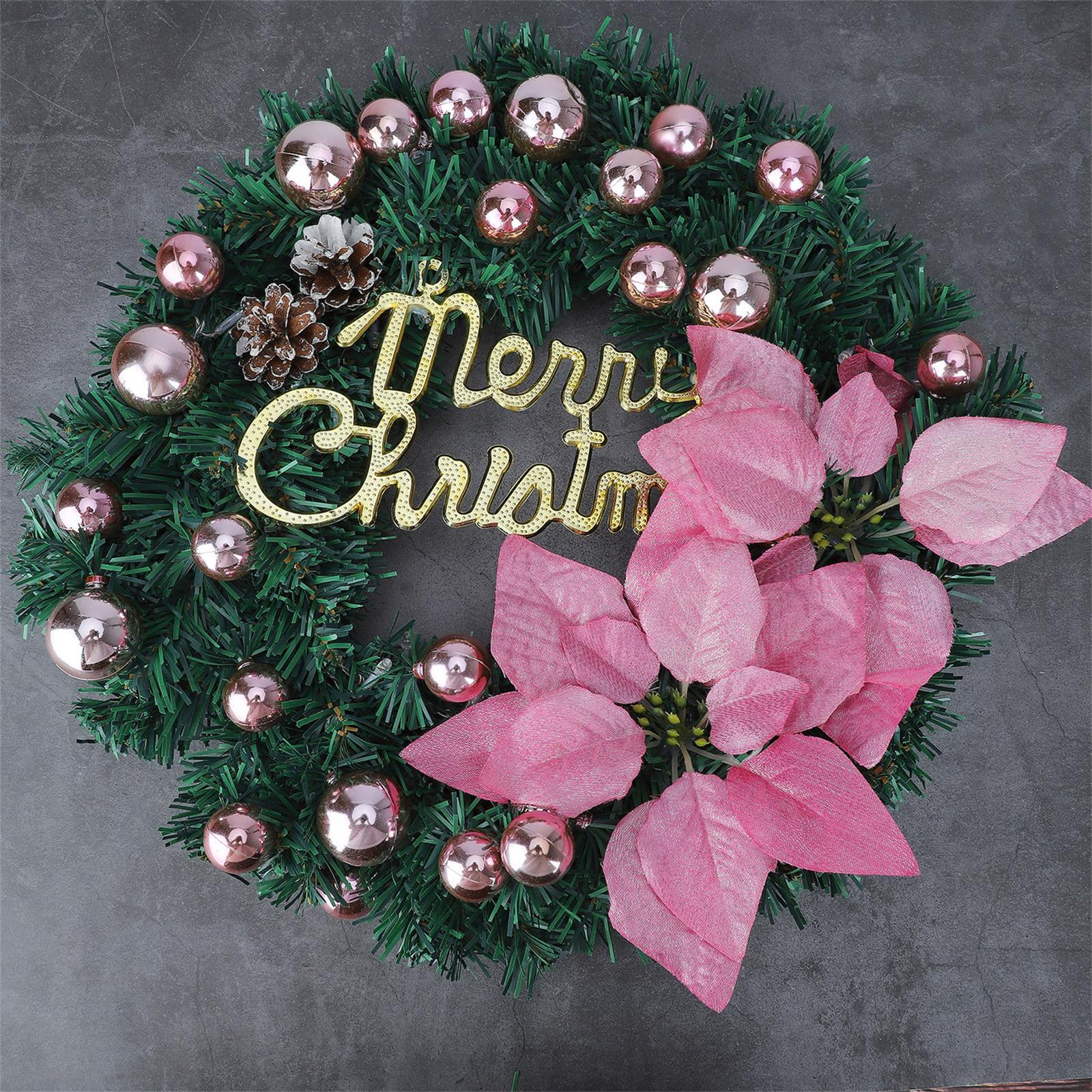 Ein Weihnachtskranz mit rosa Ornamenten, rosa Blumen und einem goldenen "Merry Christmas"-Schild auf grauem Hintergrund.