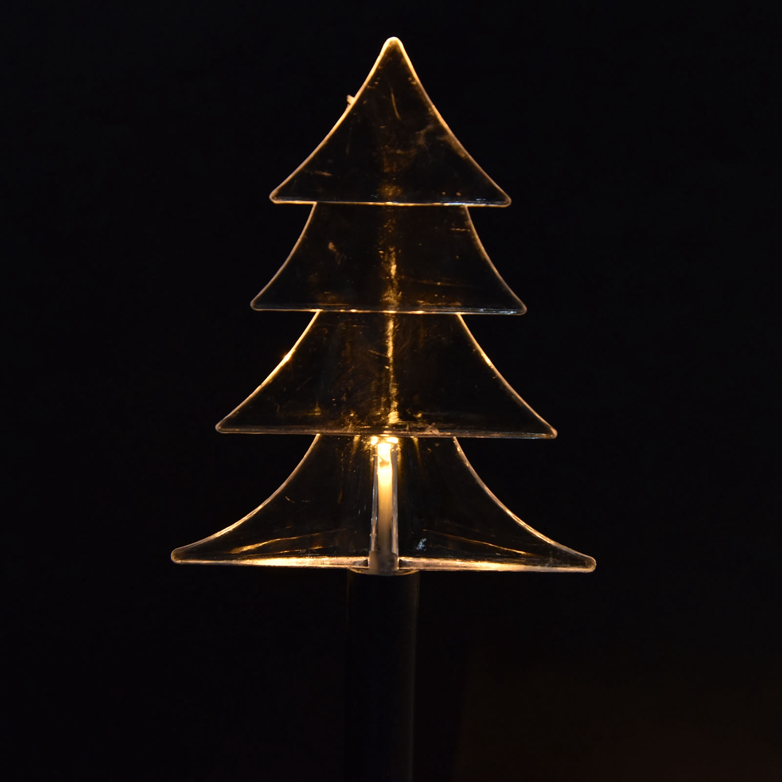 Eine transparente, geschichtete Weihnachtsbaum-förmige Leuchte leuchtet vor einem schwarzen Hintergrund. Sie wird von innen beleuchtet.