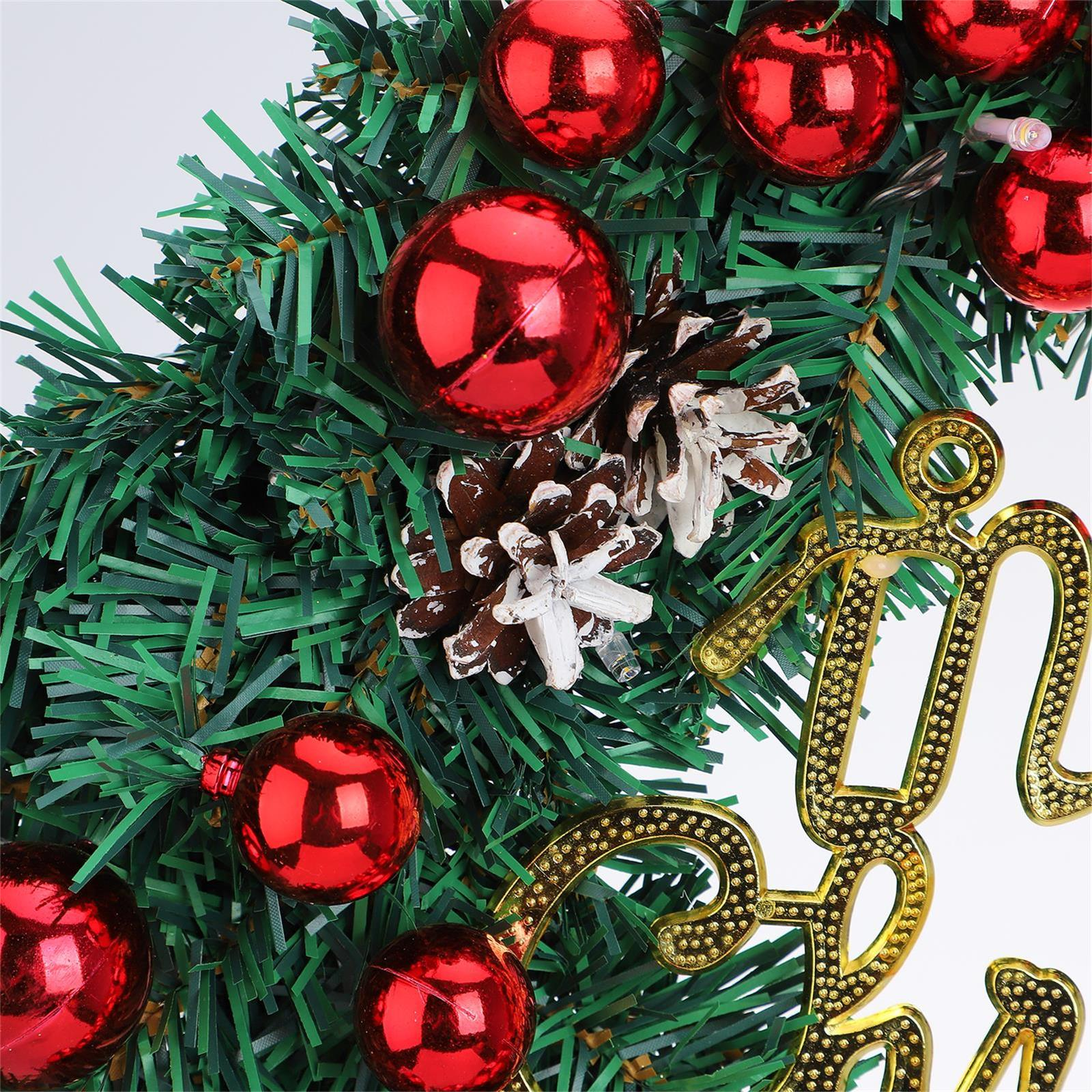 Ein Weihnachtskranz mit roten Ornamenten, Tannenzapfen und goldenem Schriftzug auf weißem Hintergrund.