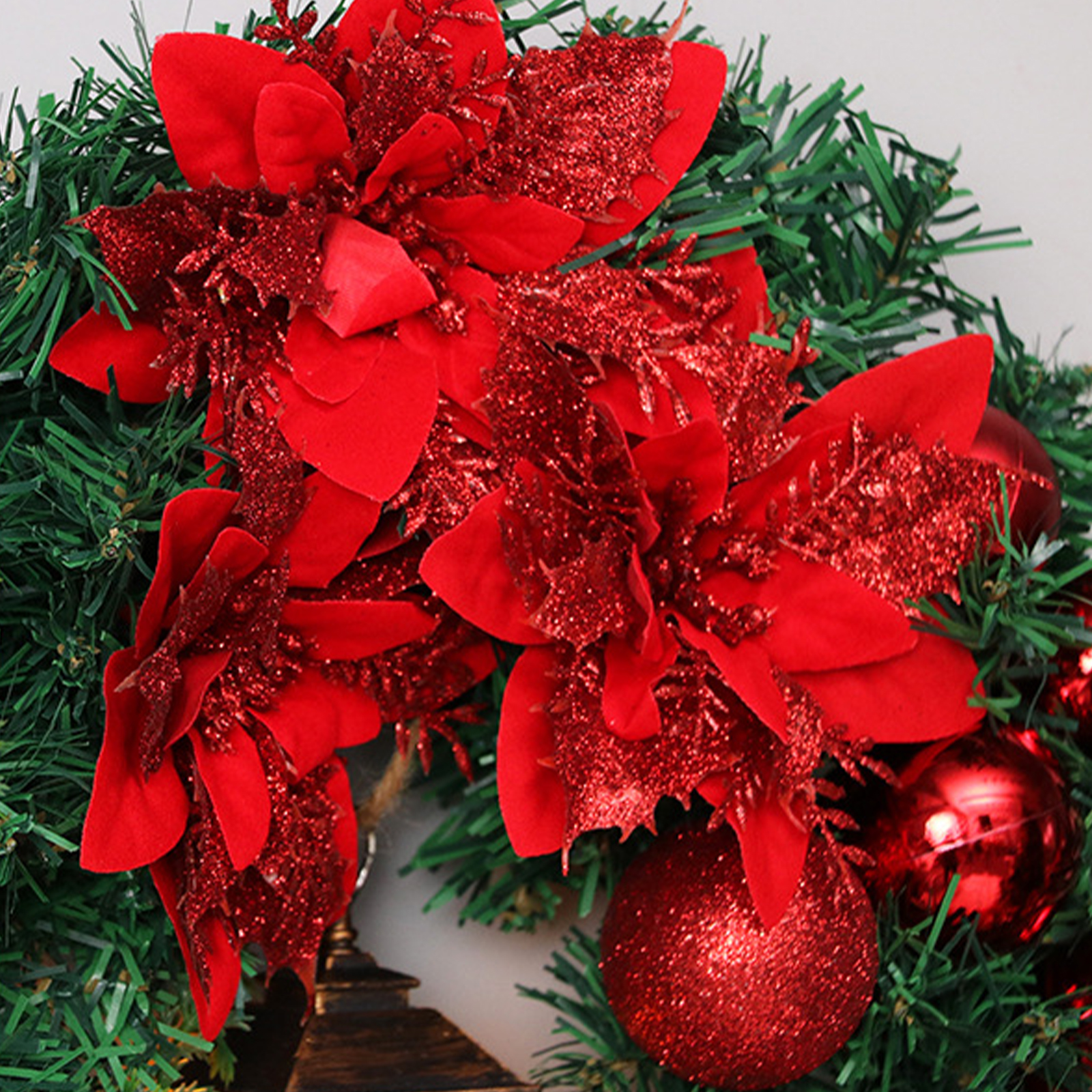 Weihnachtskranz mit roten Poinsettien und Ornamenten. Grüne Nadeln bilden die Basis. Glitzer verleiht den Dekorationen Glanz.