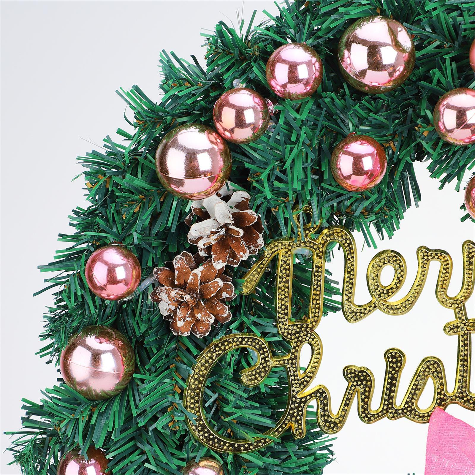 Weihnachtskranz mit grünen Nadeln, rosa Ornamenten, Tannenzapfen und goldenem "Frohe Weihnachten"-Schild.
