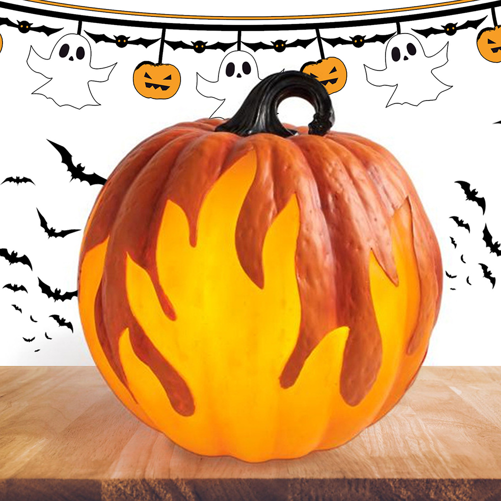 Ein leuchtender orangefarbener Kürbis mit flammenartigen Ausschnitten steht auf Holz. Halloween-Dekorationen: Fledermäuse, Geister und Kürbisse hängen darüber.