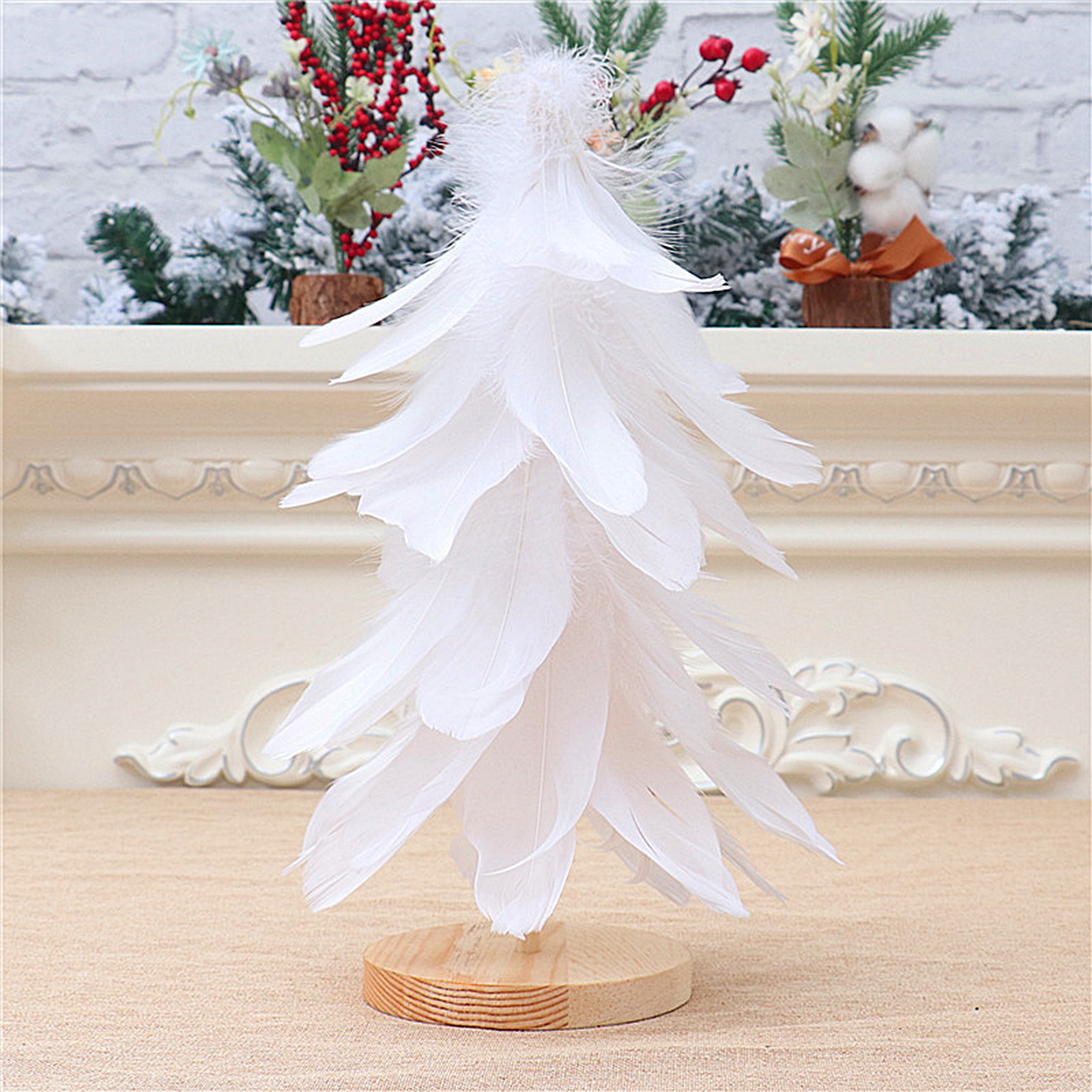 Ein weißer Feder-Weihnachtsbaum auf einem Holzsockel. Im Hintergrund Dekorationen und eine weiße Oberfläche.