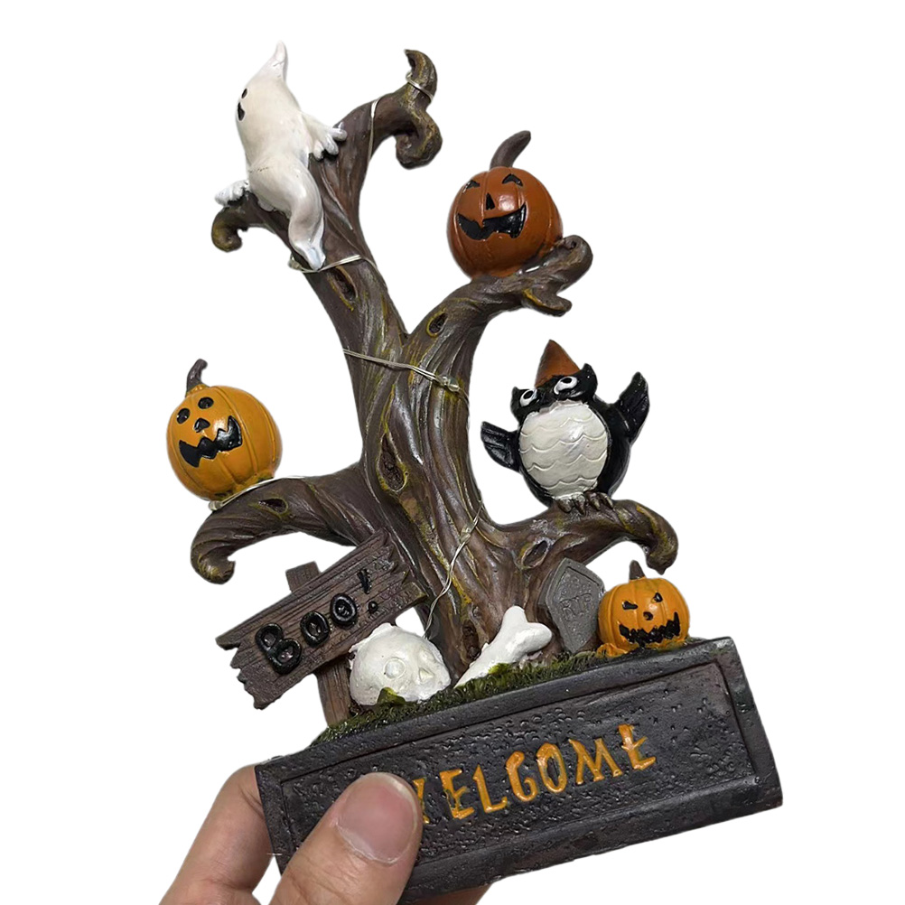 Halloween-Dekoration, die von Hand gehalten wird. Sie hat einen Baum mit einem Geist, Kürbissen und einem Vogel. Die Basis sagt 'WELCOME'.