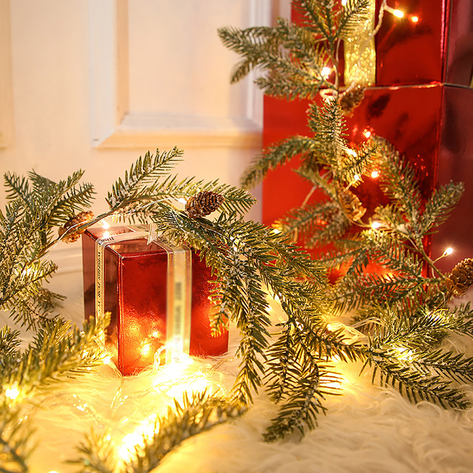 Rote Geschenkboxen mit Schleife und Kiefernzweigen mit Lichterketten auf weißer, flauschiger Oberfläche. Weihnachtsszene.
