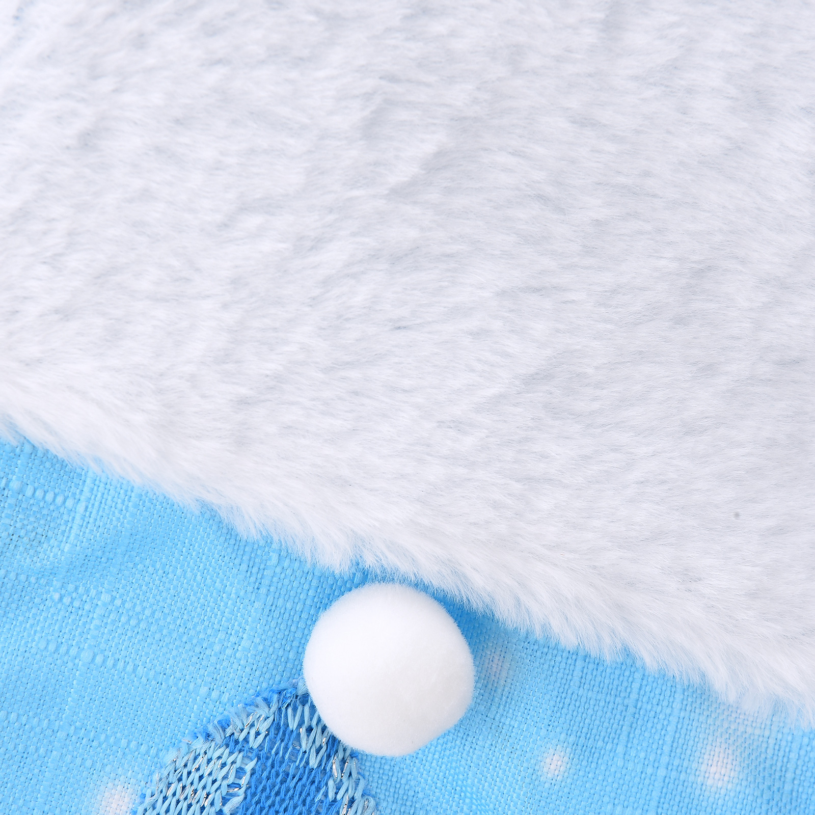 Ein weißes, flauschiges Material grenzt an einen blauen Strickstoff. Unten sitzt ein weißer Bommel. Die Stoffe wirken festlich.