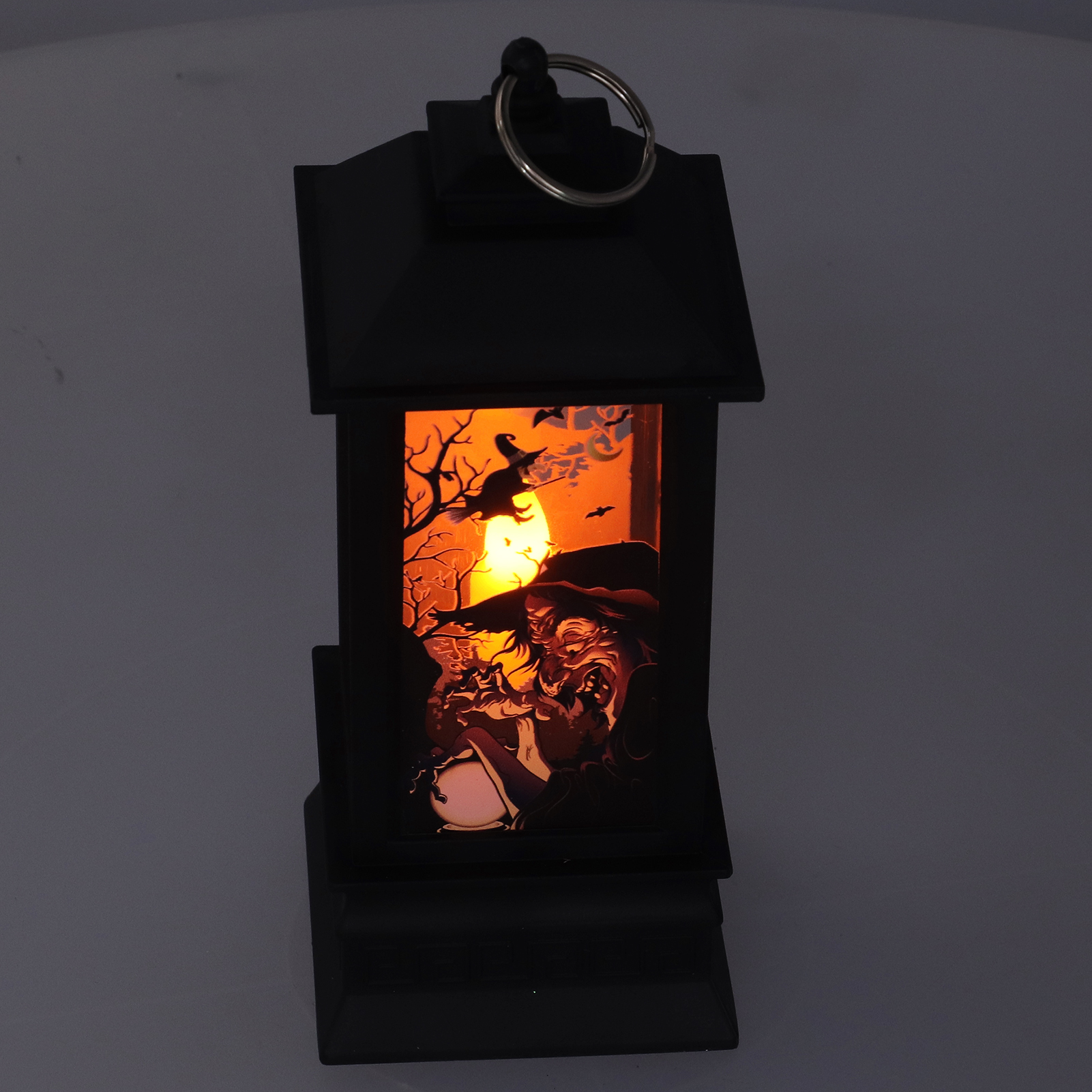 Eine schwarze Halloween-Laterne mit einer beleuchteten Hexenszene im Inneren. Eine Hexe fliegt auf einem Besen.