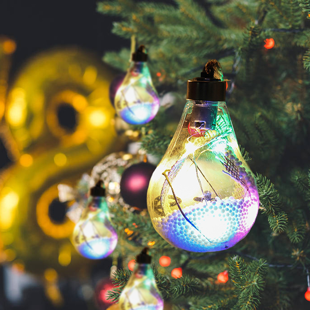 Weihnachtsbaum mit hängenden Glühbirnen-Ornamenten, gefüllt mit bunten Lichtern. Hintergrund zeigt Dekorationen und Äste.