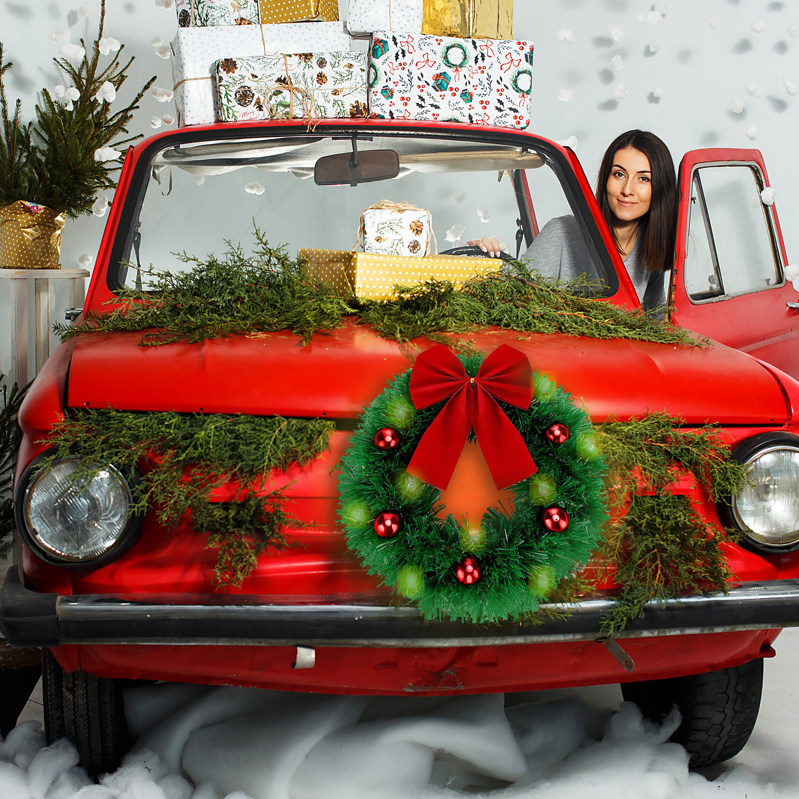 Ein rotes Auto mit Weihnachtsdekoration. Eine Frau sitzt darin. Geschenke sind obenauf gestapelt. Vorne ist ein Kranz.