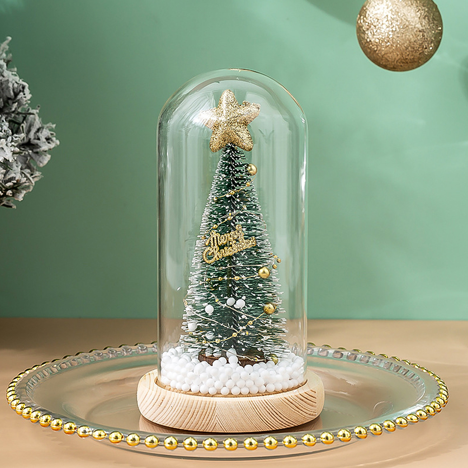 Ein Weihnachtsbaum in einer Glaskuppel mit Stern. Er steht auf einem Holzsockel auf einem dekorativen Teller. Goldene Akzente.