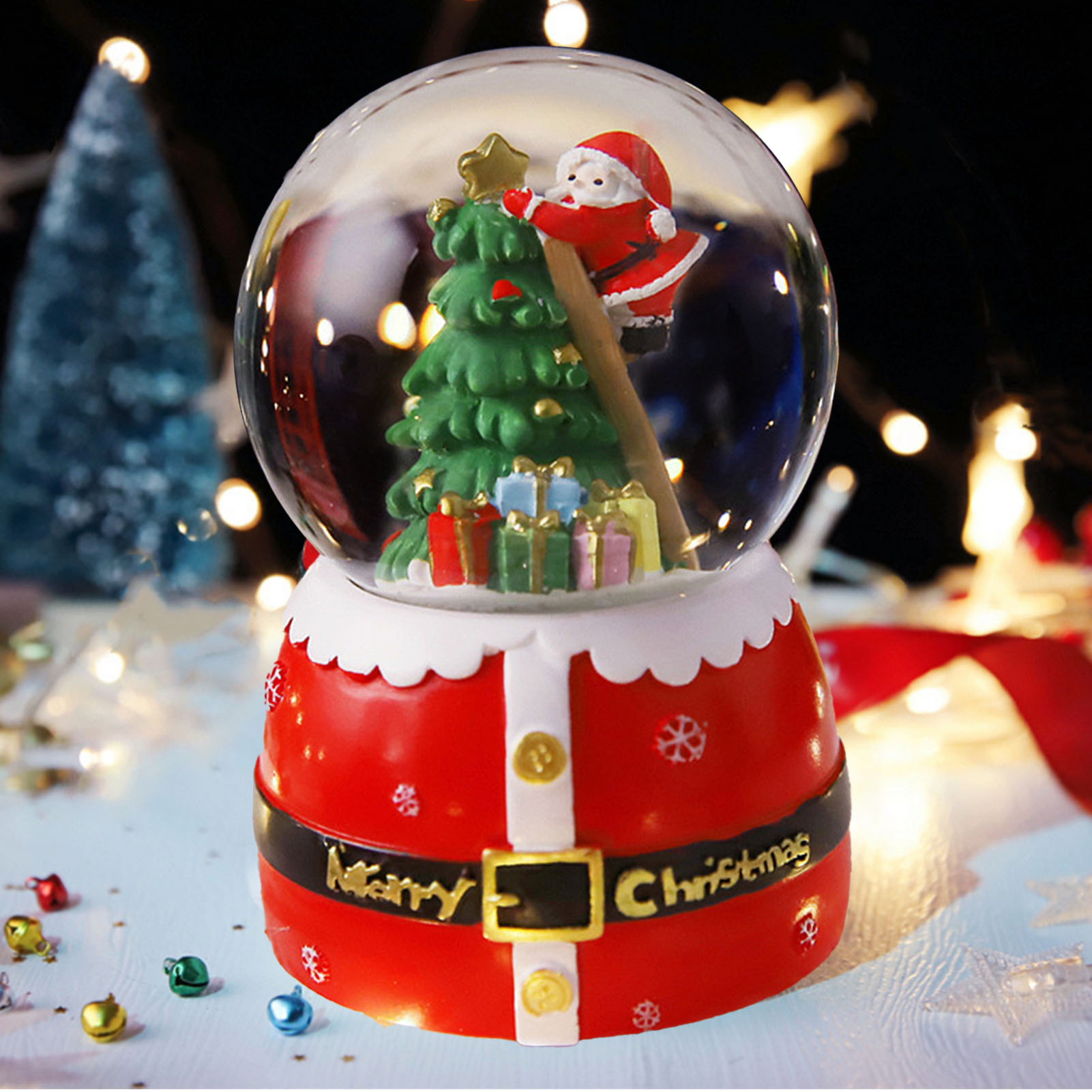 Eine Schneekugel mit Weihnachtsmann, Weihnachtsbaum und Geschenken. Der Sockel ist rot mit Gürtel und Schriftzug 'Merry Christmas'.