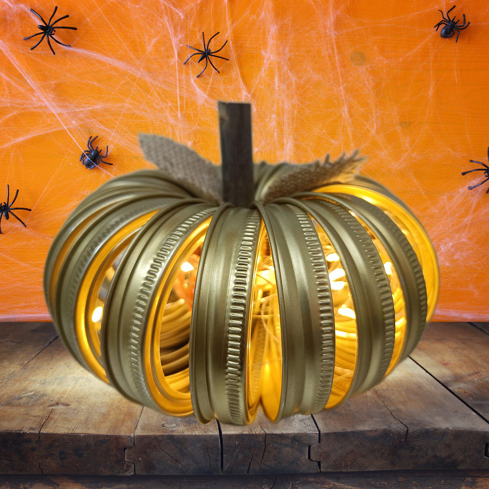 Goldener Kürbis aus Deckeln mit Lichtern, auf Holz, orangefarbener Hintergrund mit Spinnen und Spinnweben.