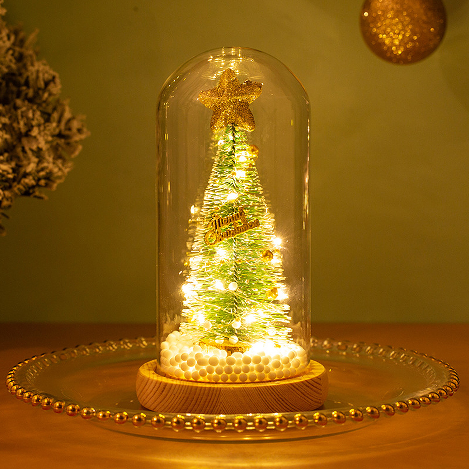 Ein Weihnachtsbaum in einer Glaskuppel, Lichter und ein Stern oben, auf einem Holzsockel, auf einer Glasplatte.