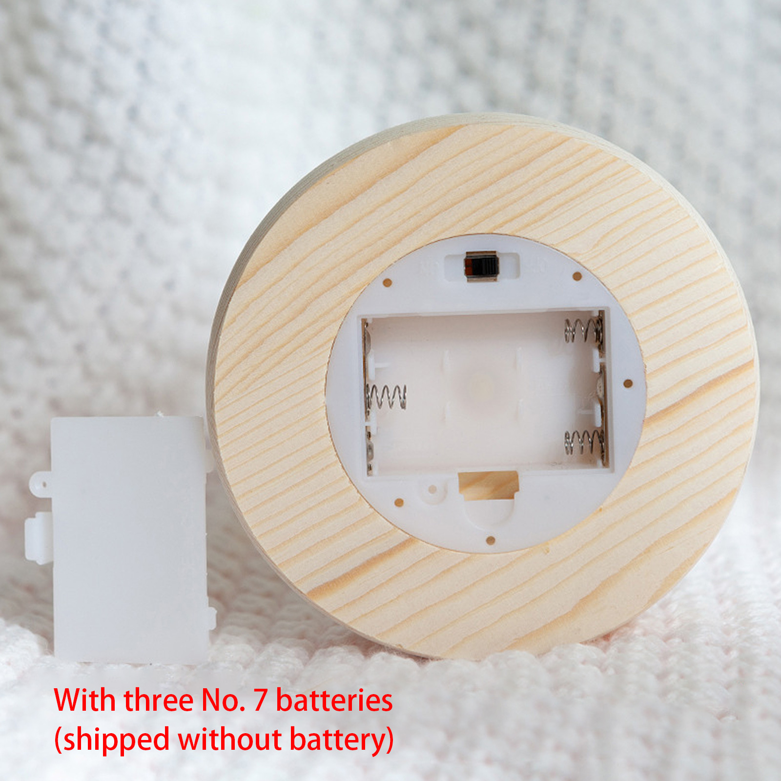 Ein Holzsockel mit Batteriefach, eine separate weiße Kunststoffabdeckung und ein weißer Strickhintergrund.