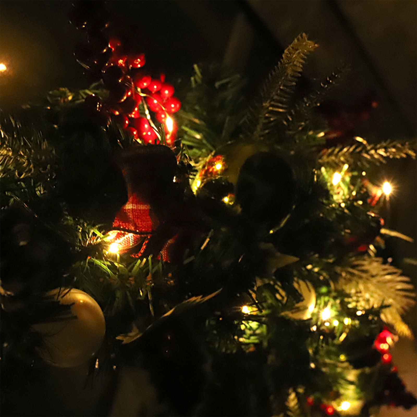 Nahaufnahme eines geschmückten Weihnachtsbaums mit roten Beeren, Lichtern und Ornamenten. Dunkler Hintergrund.