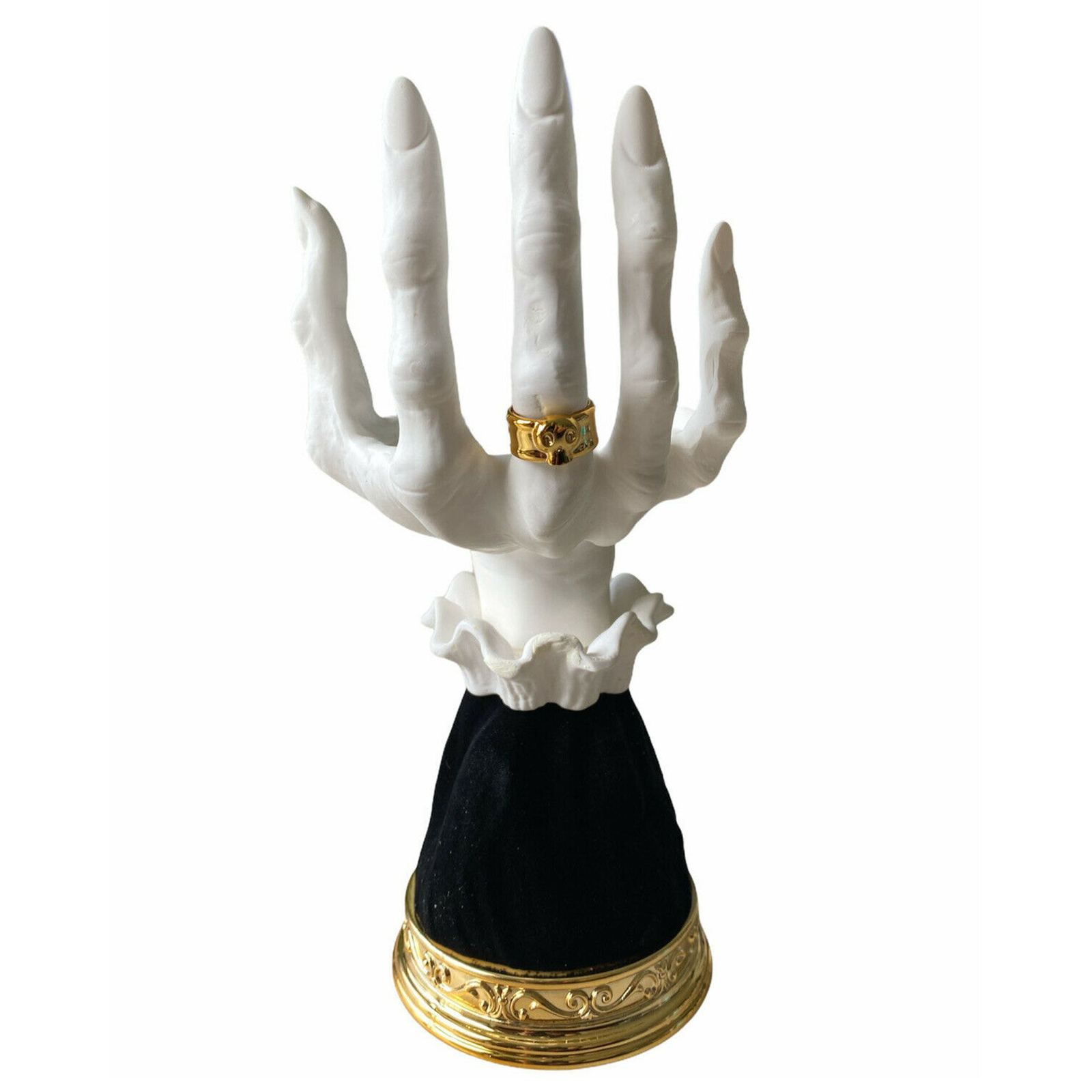 Eine weiße Handstatue mit einem goldenen Ring. Sie ruht auf einem schwarzen Samtsockel mit goldenem Rand.