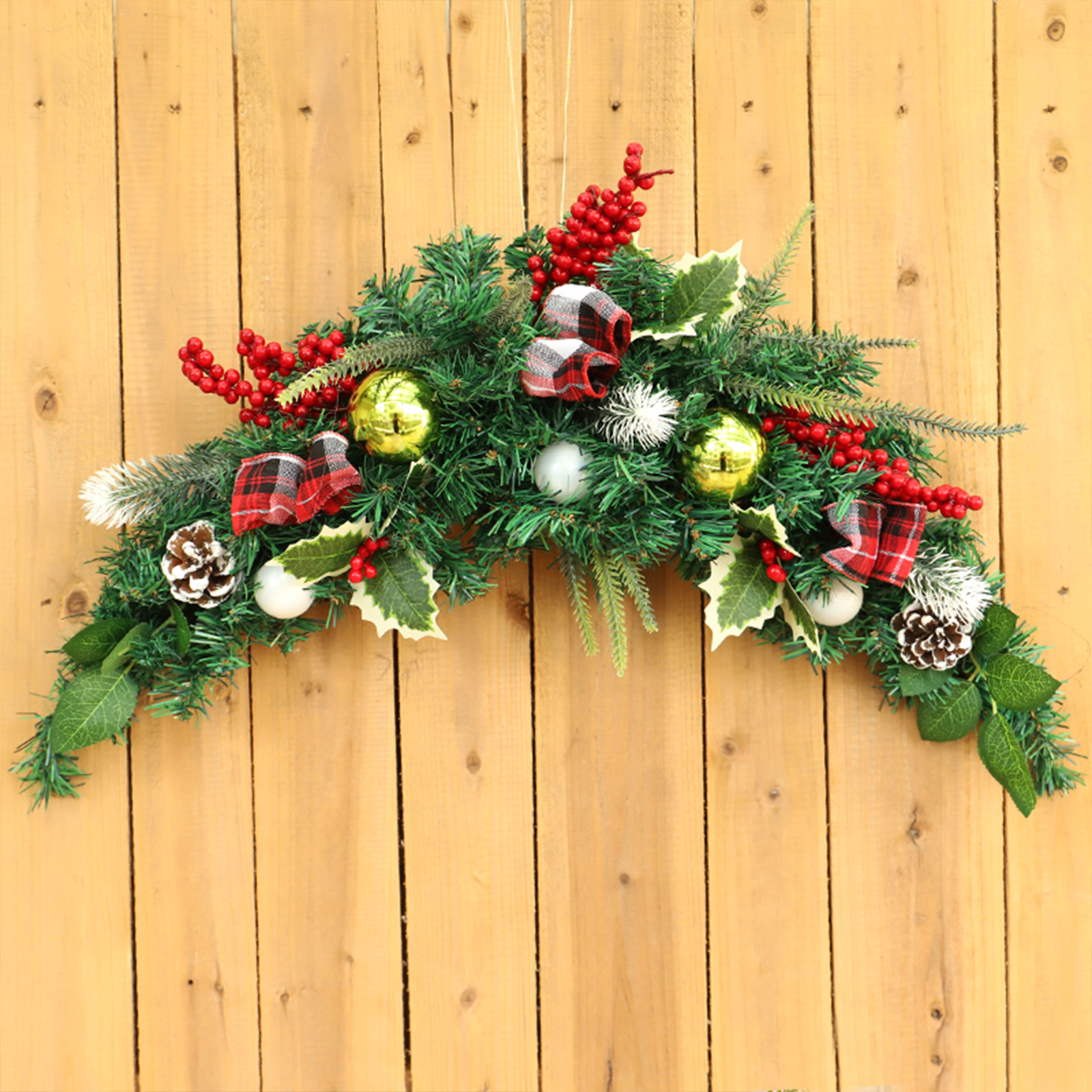 Weihnachtsdekoration auf Holzgrund. Enthält grünes Tannengrün, rote Beeren, goldene Kugeln, weiße Ornamente und karierte Bänder.