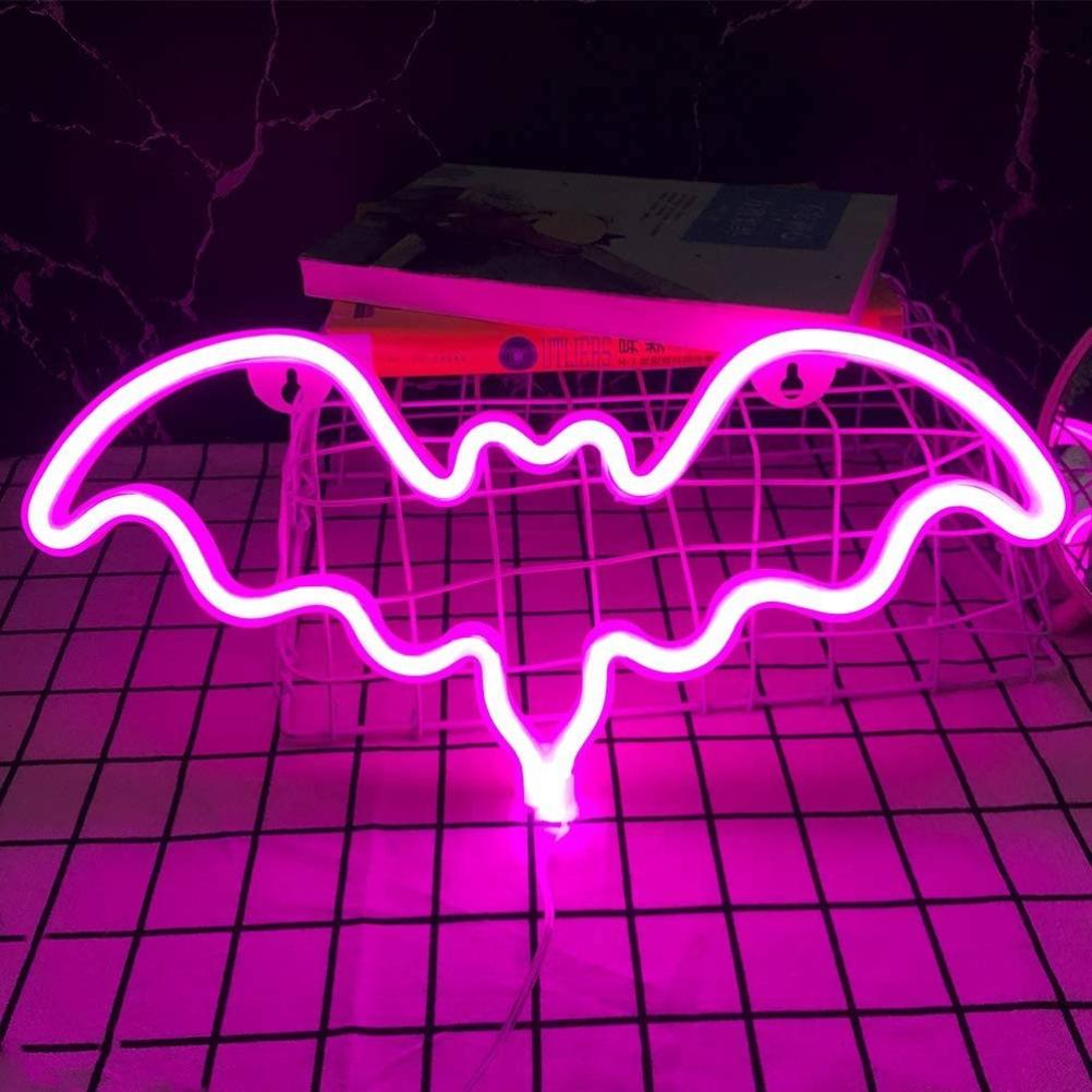 Ein pinkfarbenes Neon-Fledermausschild leuchtet. Im Hintergrund liegen Bücher auf einem weißen Drahtkorb, vor einem schwarz-weiß karierten Untergrund.