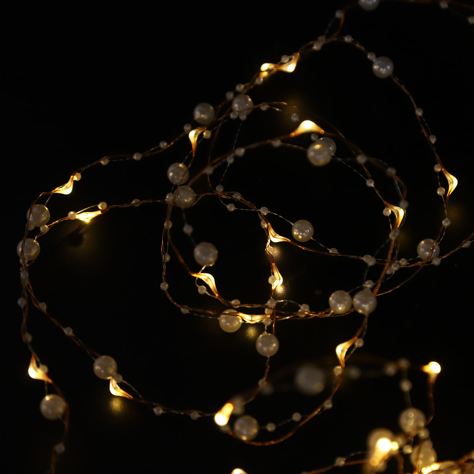 Schnur aus perlenartigen Perlen und kleinen Lichtern auf dunklem Hintergrund. Die Lichter sind warm getönt.
