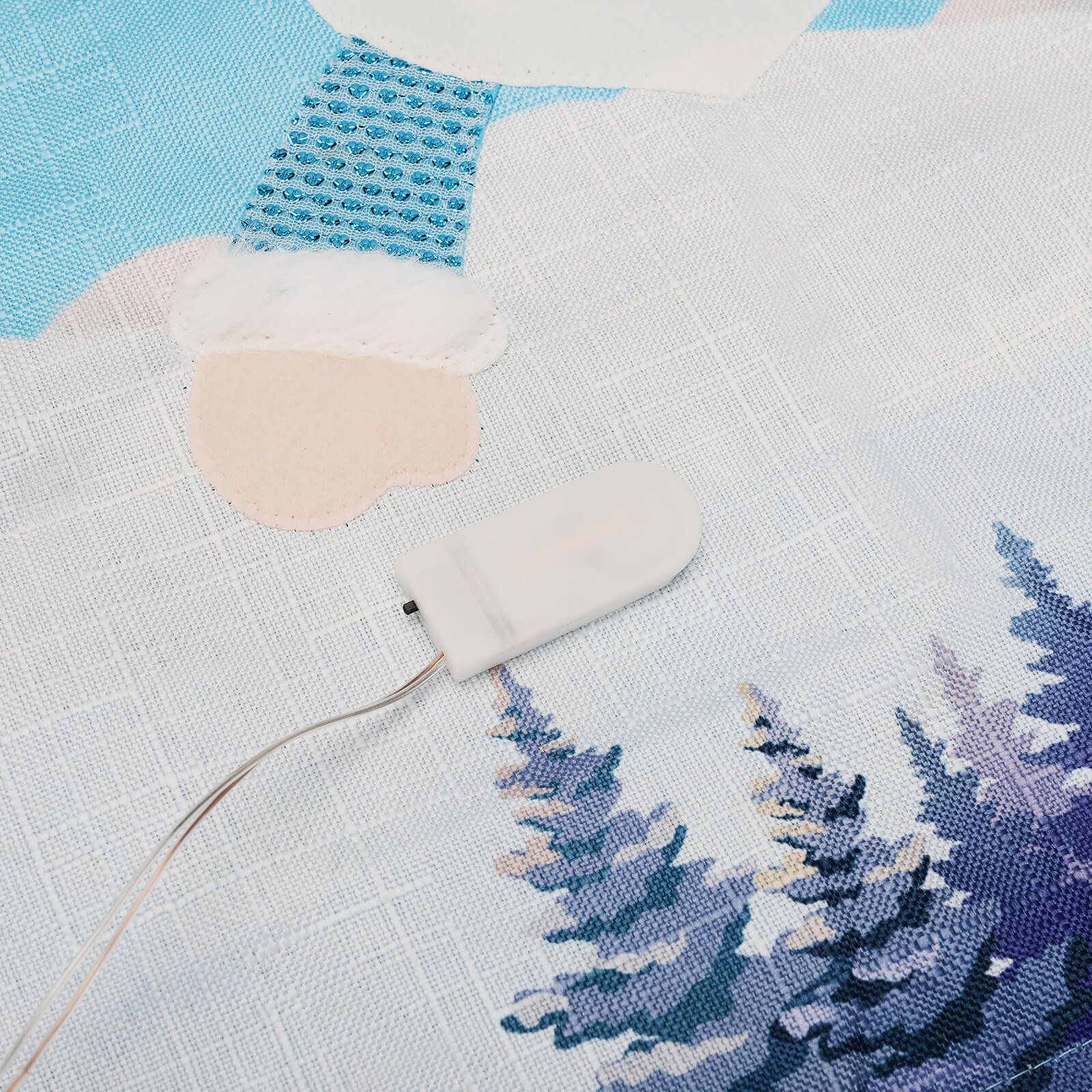 Ein dekorierter Stoff zeigt ein Licht, ein Schneemann-Detail und eine Waldszene in Blau und Weiß.