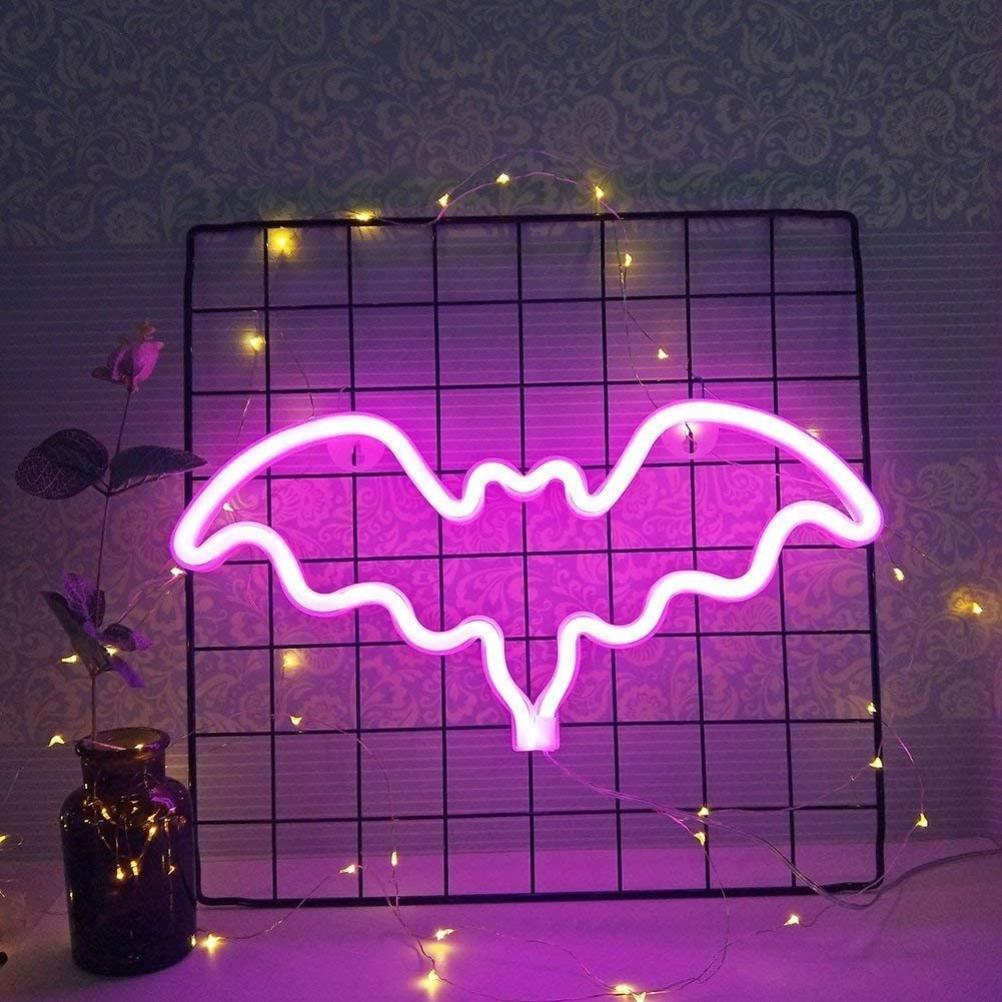 Ein neonfarbenes Fledermausschild leuchtet pink vor einem schwarzen Gitter. Lichterketten und eine kleine Flasche befinden sich im Vordergrund, und Tapeten im Hintergrund.