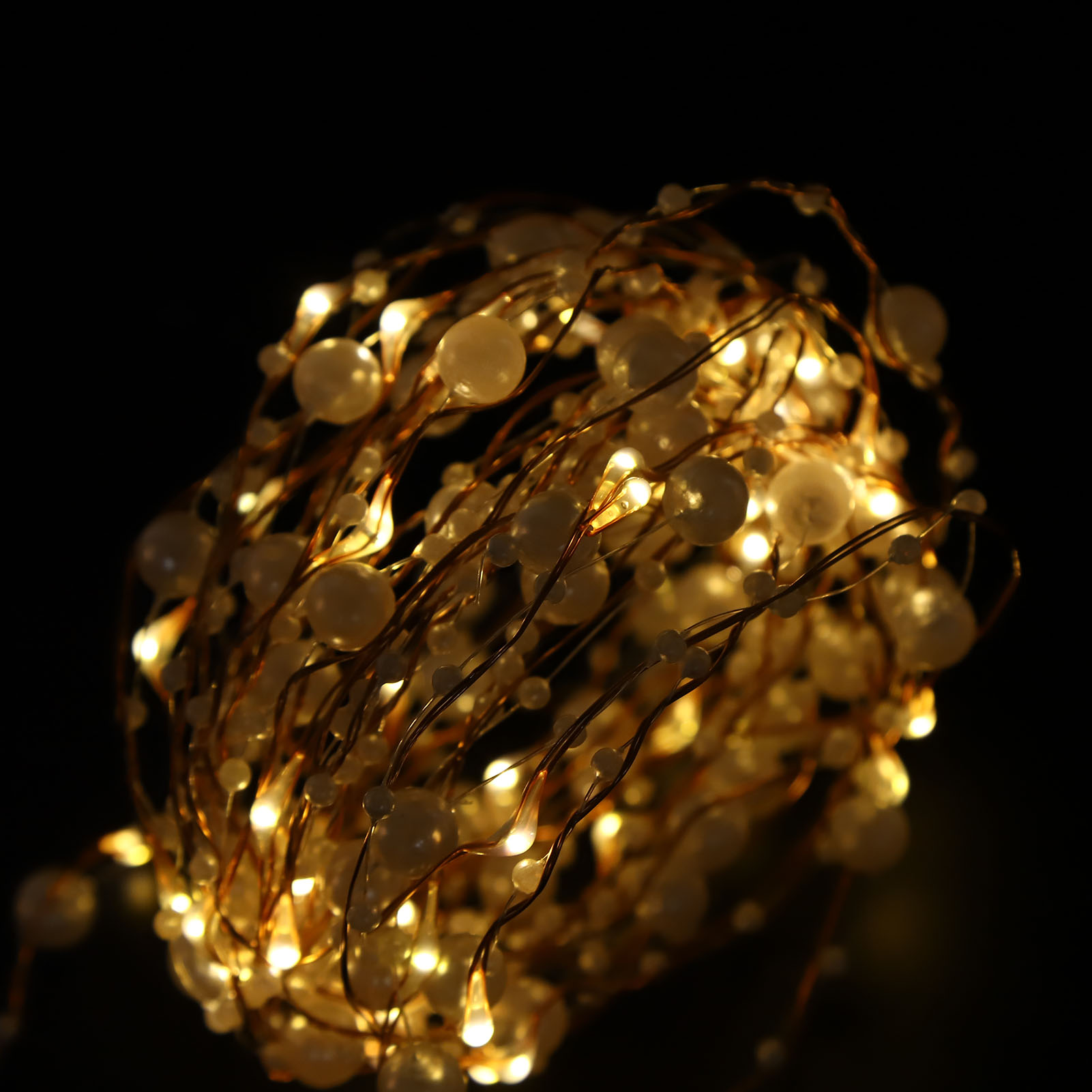Schnur aus warmen LED-Leuchten mit weißen, perlenartigen Glühbirnen auf Kupferdraht vor schwarzem Hintergrund. Die Lichter sind an.