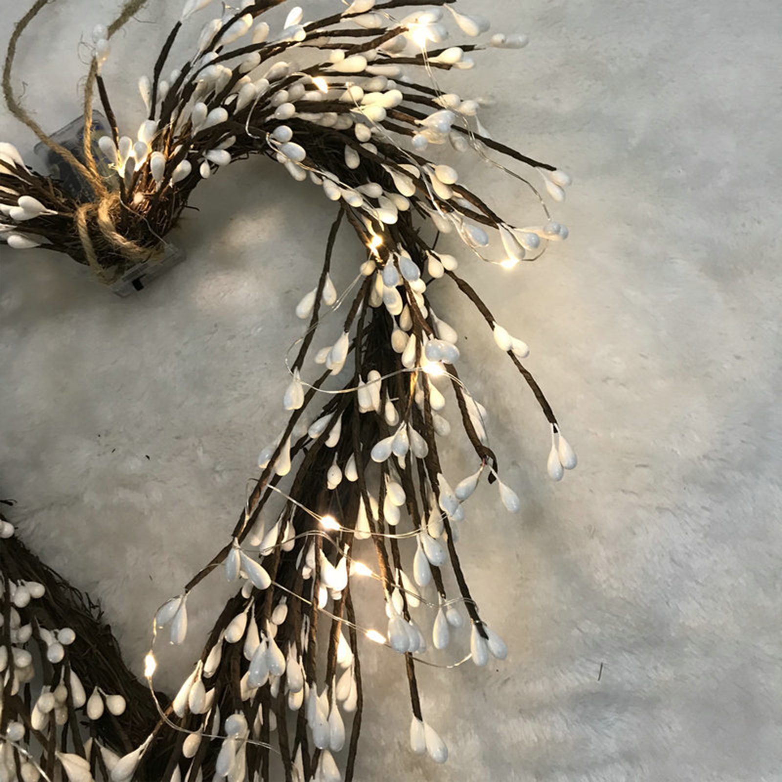 Ein herzförmiger Kranz mit weißen, tropfenförmigen Ornamenten. Überall sind funkelnde Lichter angebracht. Der Hintergrund ist flauschig weiß.