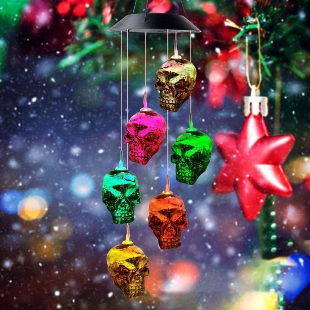 Ein Windspiel mit bunten Schädelornamenten hängt vor einem verschwommenen Hintergrund aus Weihnachtsdekorationen und fallendem Schnee.