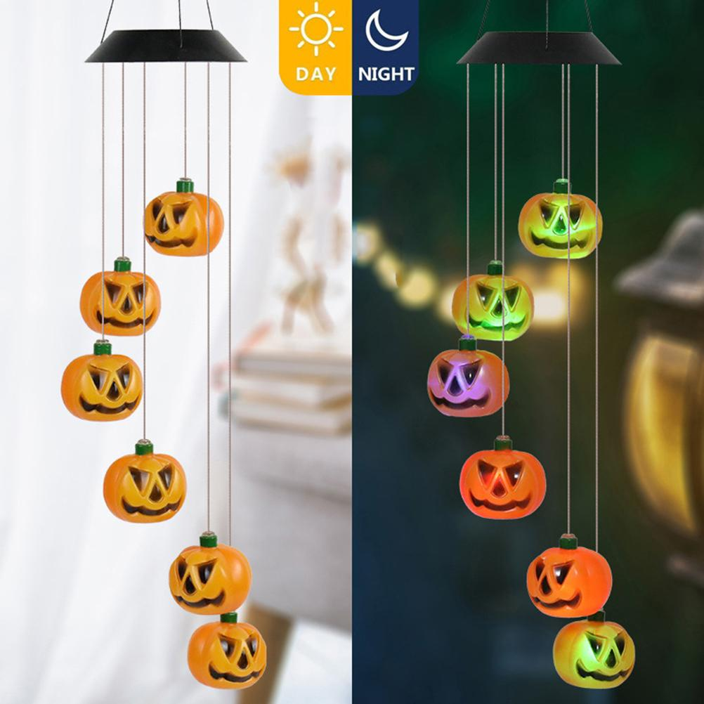 Ein Halloween-Windspiel mit orangefarbenen Kürbislichtern. Die linke Seite zeigt Kürbisse bei Tageslicht, die rechte Seite leuchtet nachts.