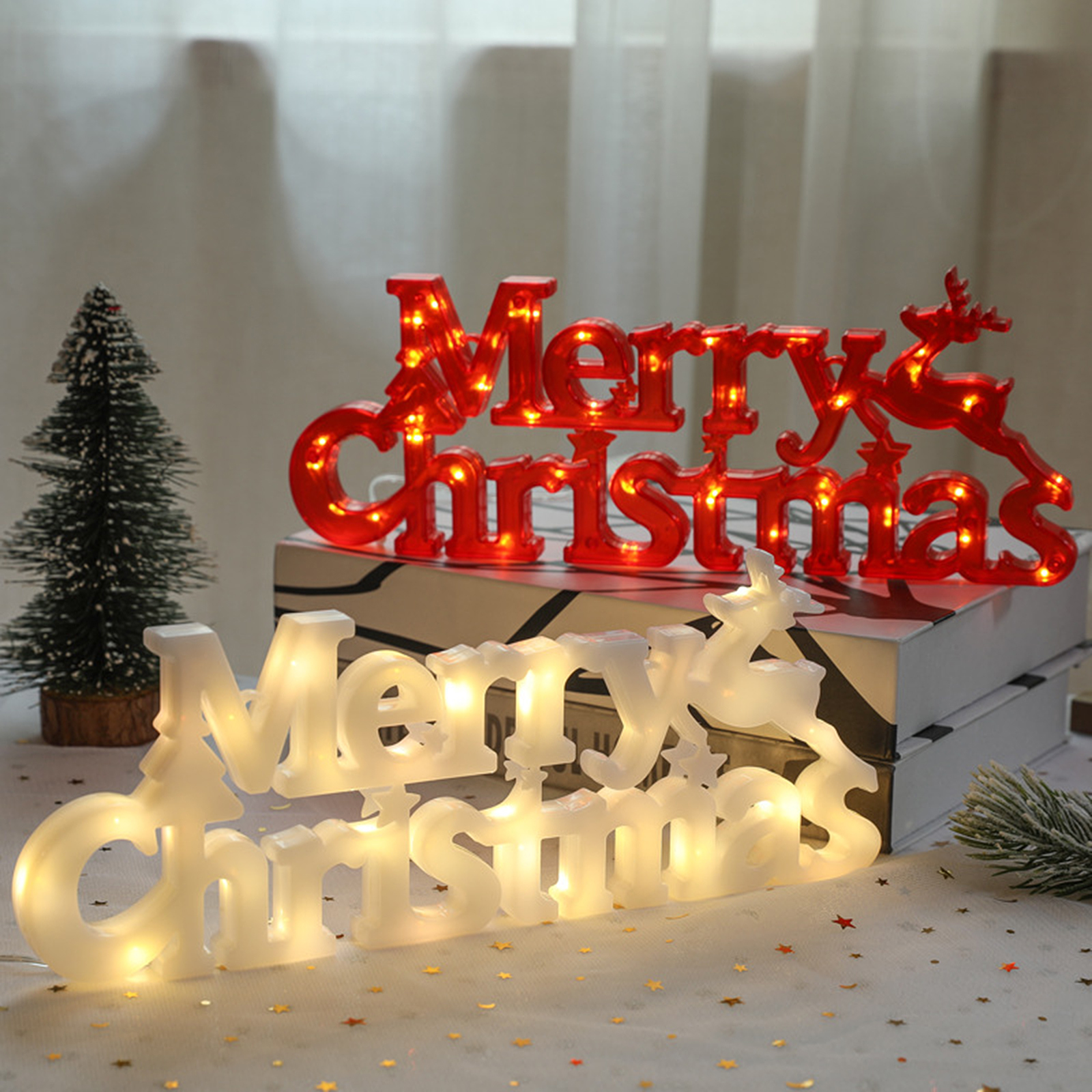 Weihnachtsdekorationen: rote und weiße beleuchtete 'Merry Christmas'-Schilder, ein kleiner Baum und eine weiße Oberfläche mit Sternen.