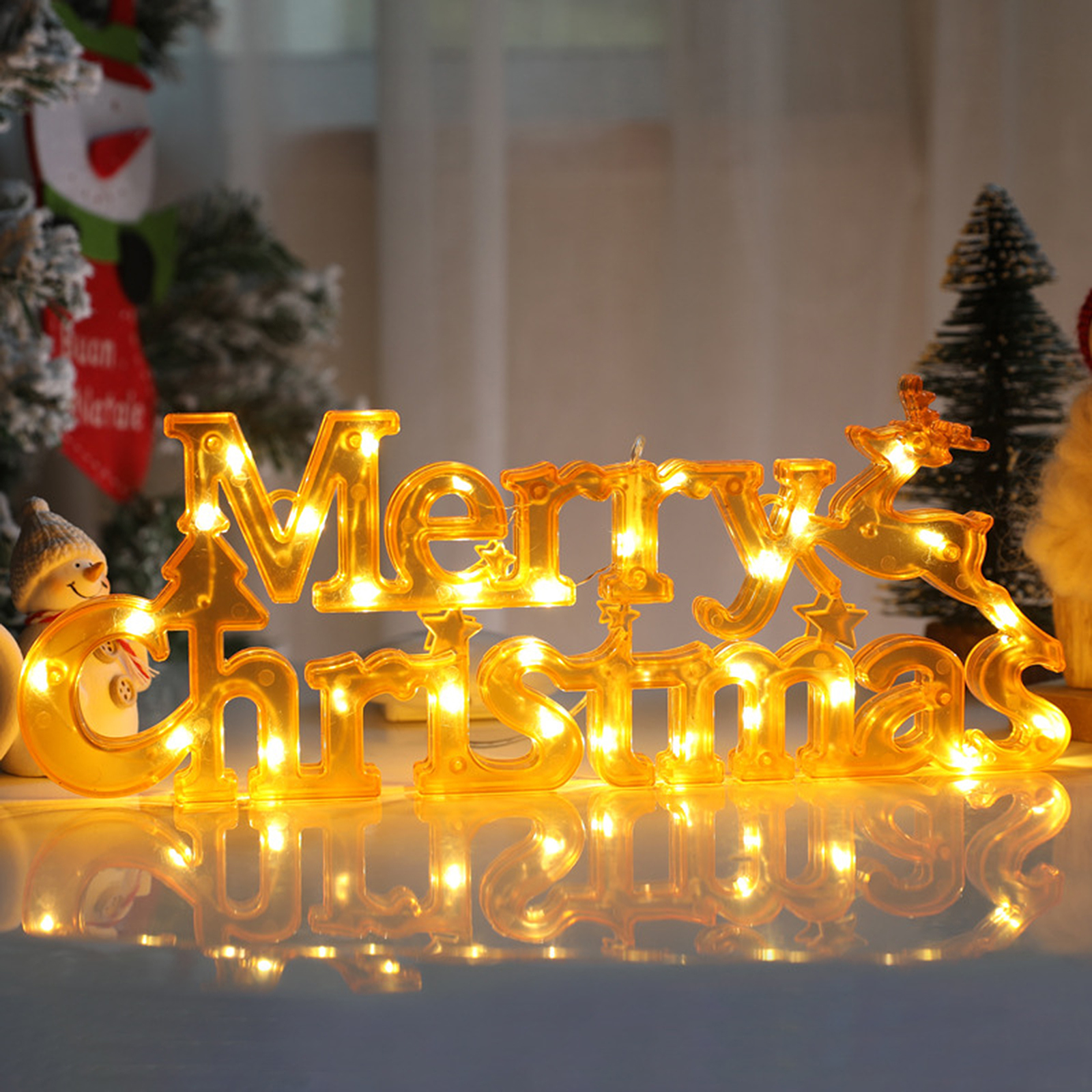 Ein beleuchtetes 'Merry Christmas'-Schild in Gold mit einem Rentier. Weitere Weihnachtsdekorationen sind im Hintergrund.