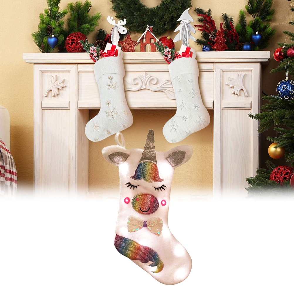 Weihnachtssocken auf einem Kaminsims, darunter ein Einhorn-Design. Weihnachtsbaum und Dekorationen sind im Hintergrund zu sehen.