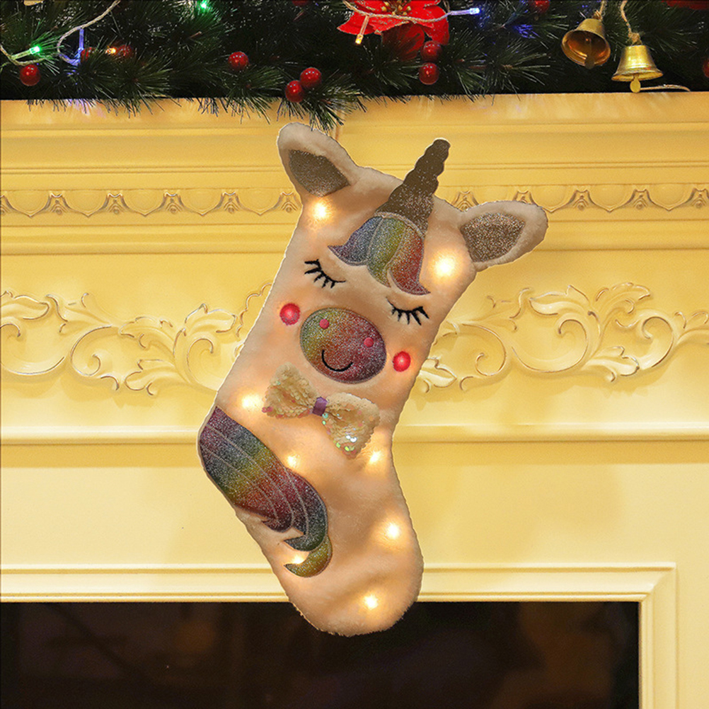 Ein weihnachtlicher Strumpf in Form eines Einhorns hängt am Kamin. Dekoriert mit Lichtern und Regenbogen-Details, mit Schleife und geschlossenen Augen.