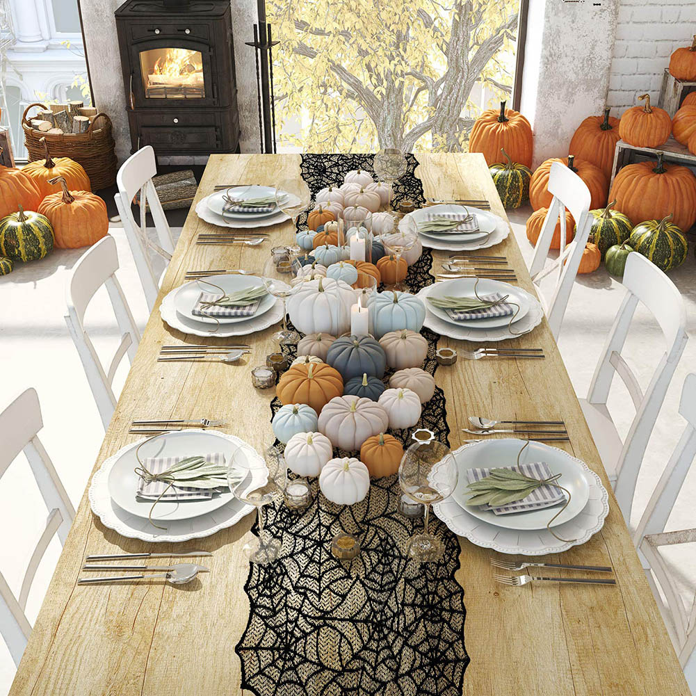 Ein Holztisch für ein Halloween-Dinner, geschmückt mit Kürbissen, Kerzen und einem schwarzen Spinnennetz-Läufer. Weiße Stühle umgeben ihn.