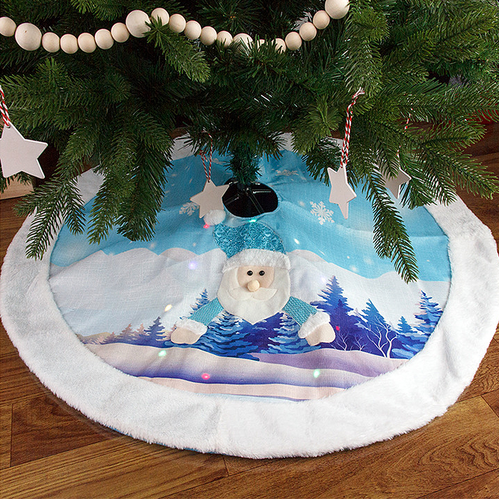 Ein Weihnachtsbaumrock mit einem Weihnachtsmann-Design liegt unter einem Baum. Der Rock hat eine Winterlandschaft und einen flauschigen weißen Rand.