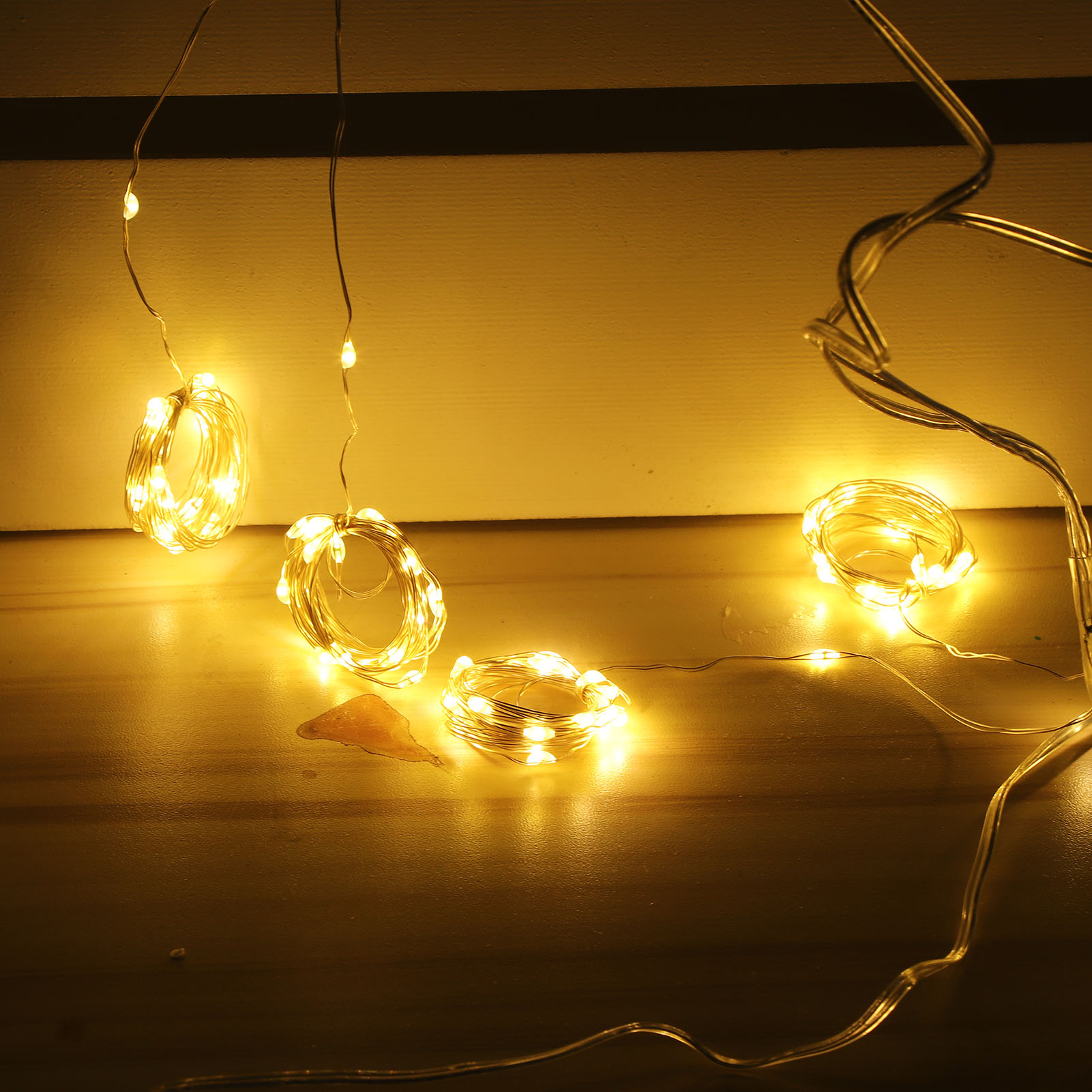 Warmweiße Lichterketten auf Holzoberfläche, einige Lichter hängen von oben. Ein kleines Objekt liegt auf der Oberfläche.