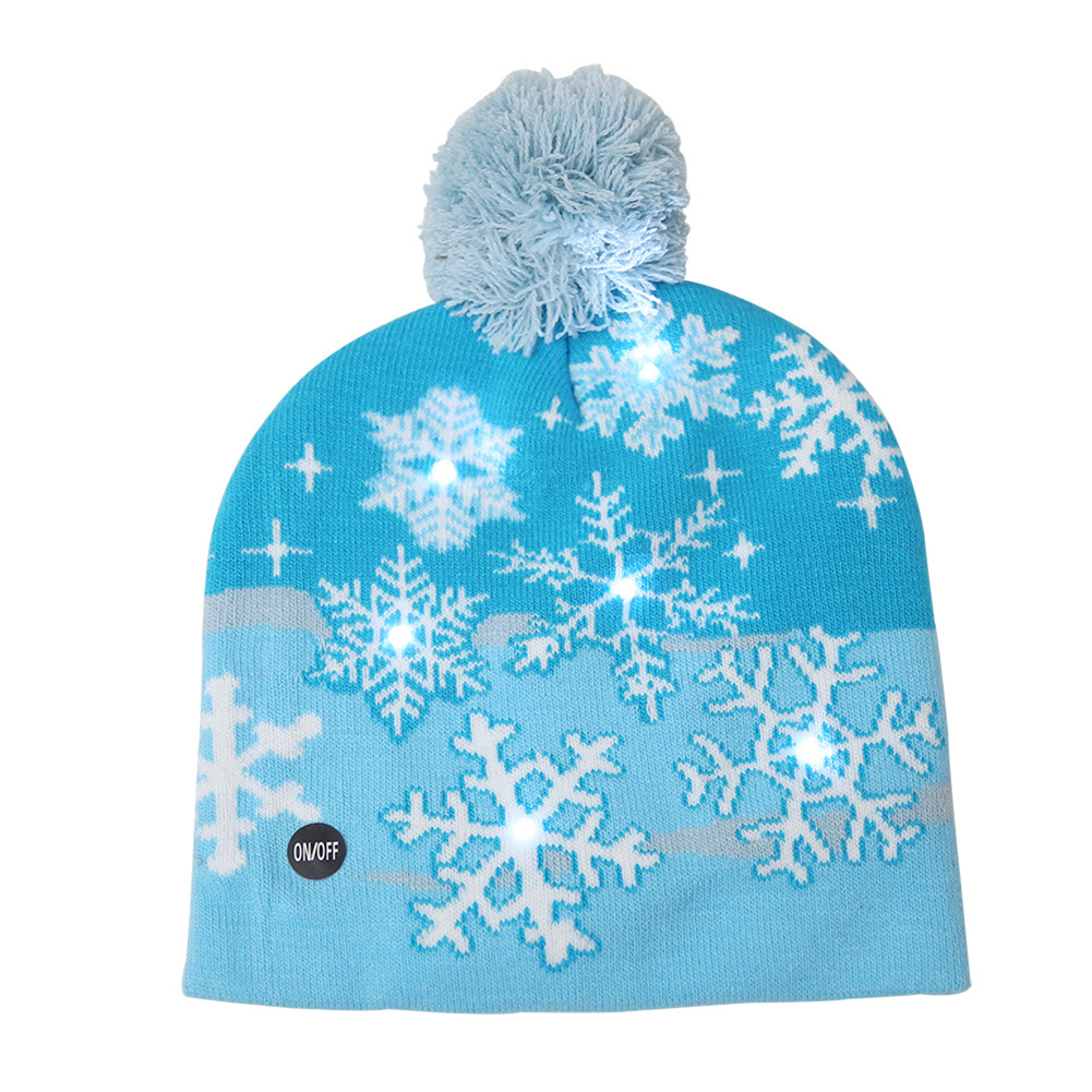 Eine blaue Strickmütze mit weißen Schneeflocken und einem Bommel. Die Mütze hat einen Ein-/Aus-Knopf und leuchtende Lichter.