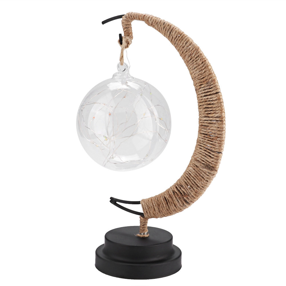 Eine dekorative Lampe mit einer Glaskugel, gefüllt mit Lichtern. Sie hängt an einem gebogenen, seilumwickelten Metallrahmen auf einem schwarzen Sockel.