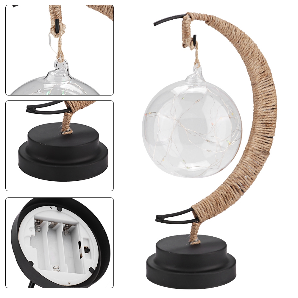 Eine dekorative Lampe mit einer Glaskugel mit Lichtern, die an einem juteumwickelten Metallrahmen auf einem schwarzen Sockel hängt.
