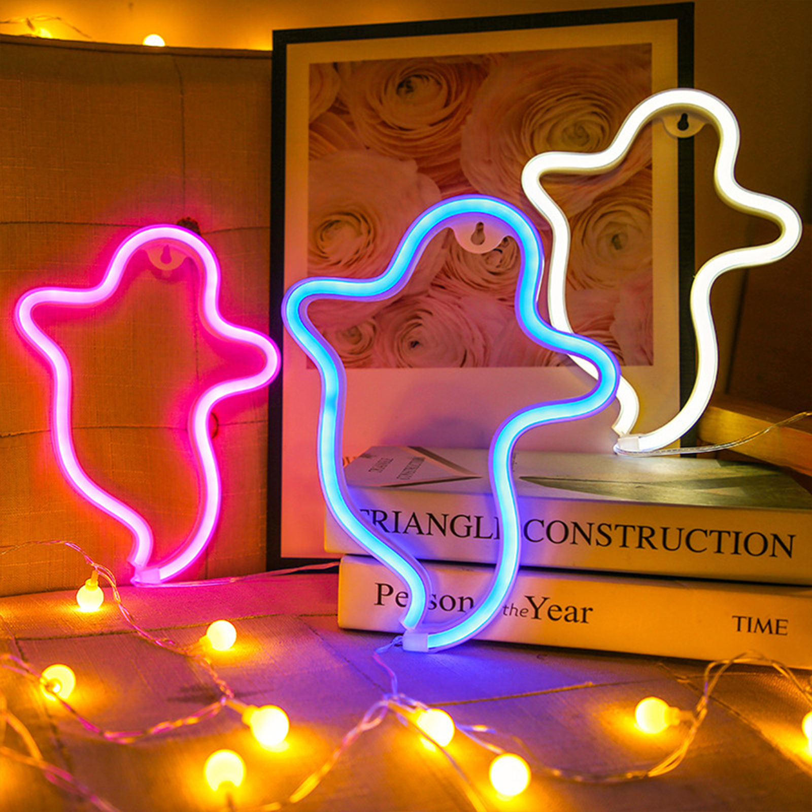 Neon-Geisterlichter in Pink, Blau und Weiß. Bücher und Lichterketten in der Szene. Rosenbild im Hintergrund.