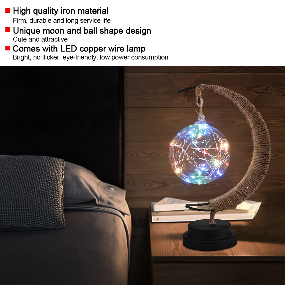 Eine dekorative Lampe mit mondförmigem Rahmen und Glaskugel mit bunten LED-Lichtern, platziert auf einem Nachttisch neben einem Bett.