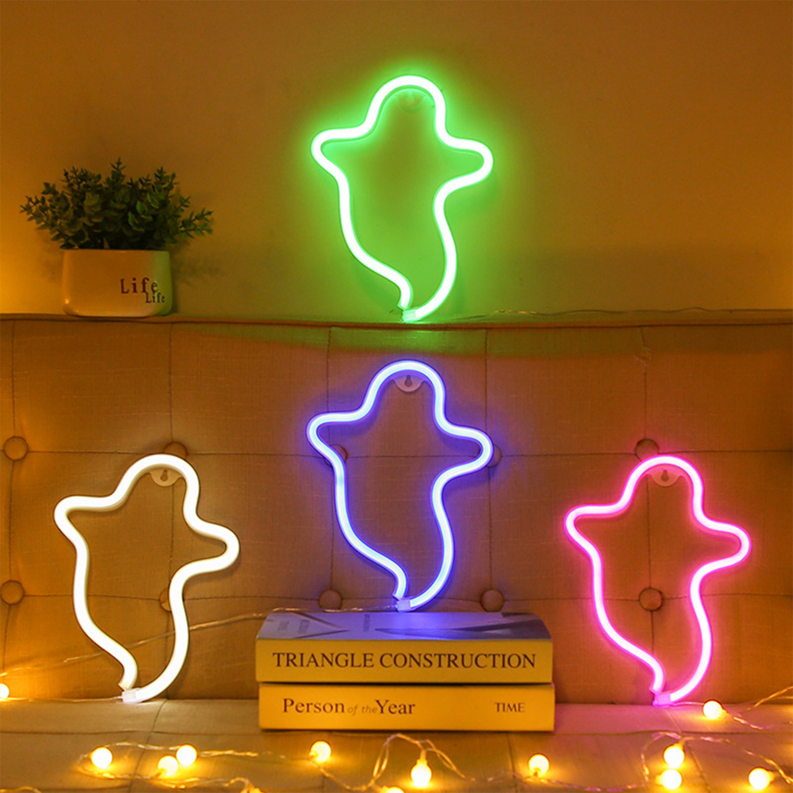 Neon-Geisterlichter in Grün, Blau, Pink und Weiß, mit einer Pflanze, Büchern und Lichterketten auf einer Oberfläche.