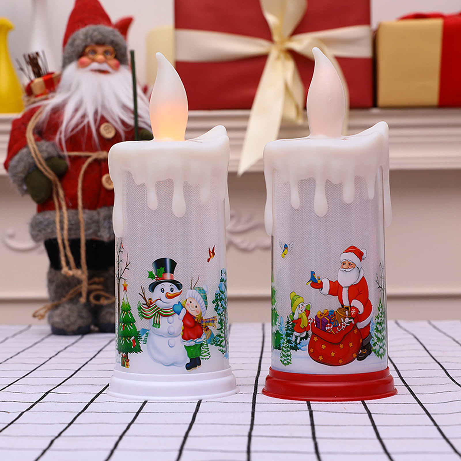Zwei Weihnachtskerzenlichter mit Schneemann- und Weihnachtsmann-Illustrationen. Eine Weihnachtsmannfigur befindet sich im Hintergrund.