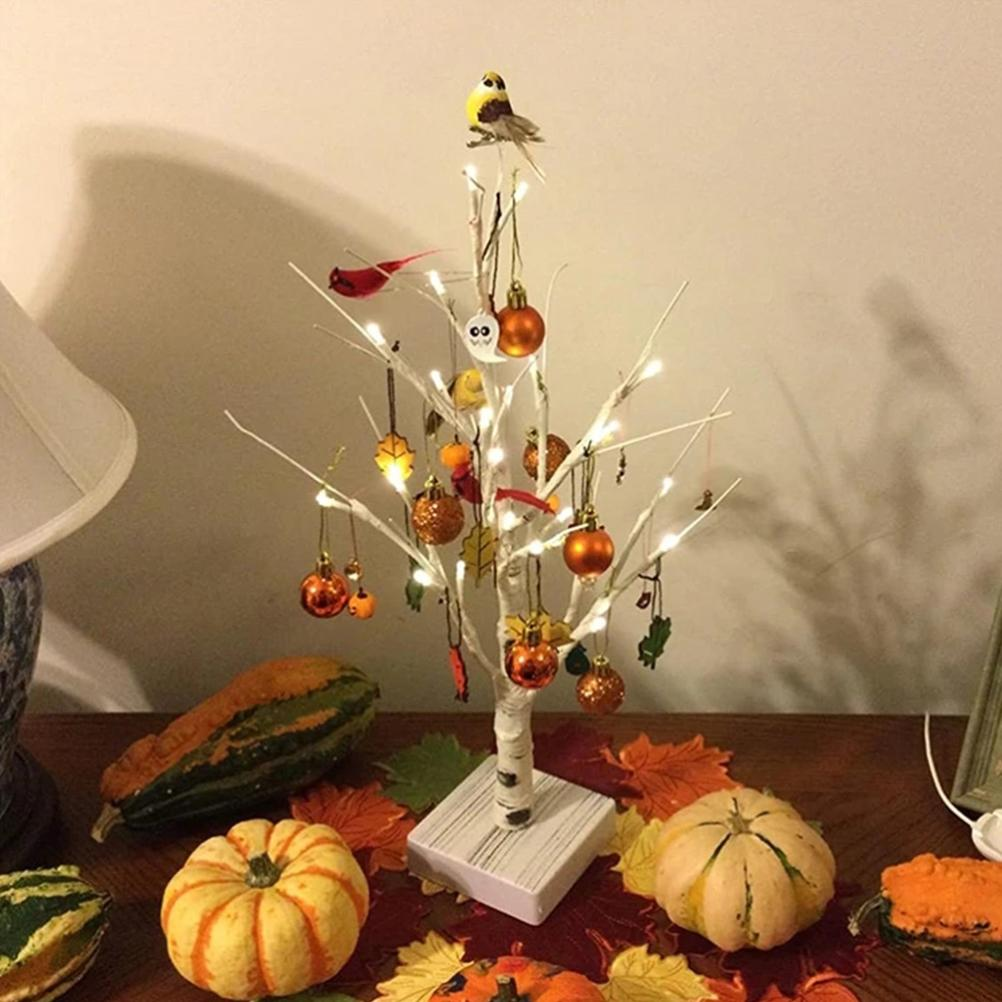 Ein kleiner dekorativer Baum mit Ornamenten und einem Vogel, umgeben von Kürbissen und Zierkürbissen auf einem Tisch.