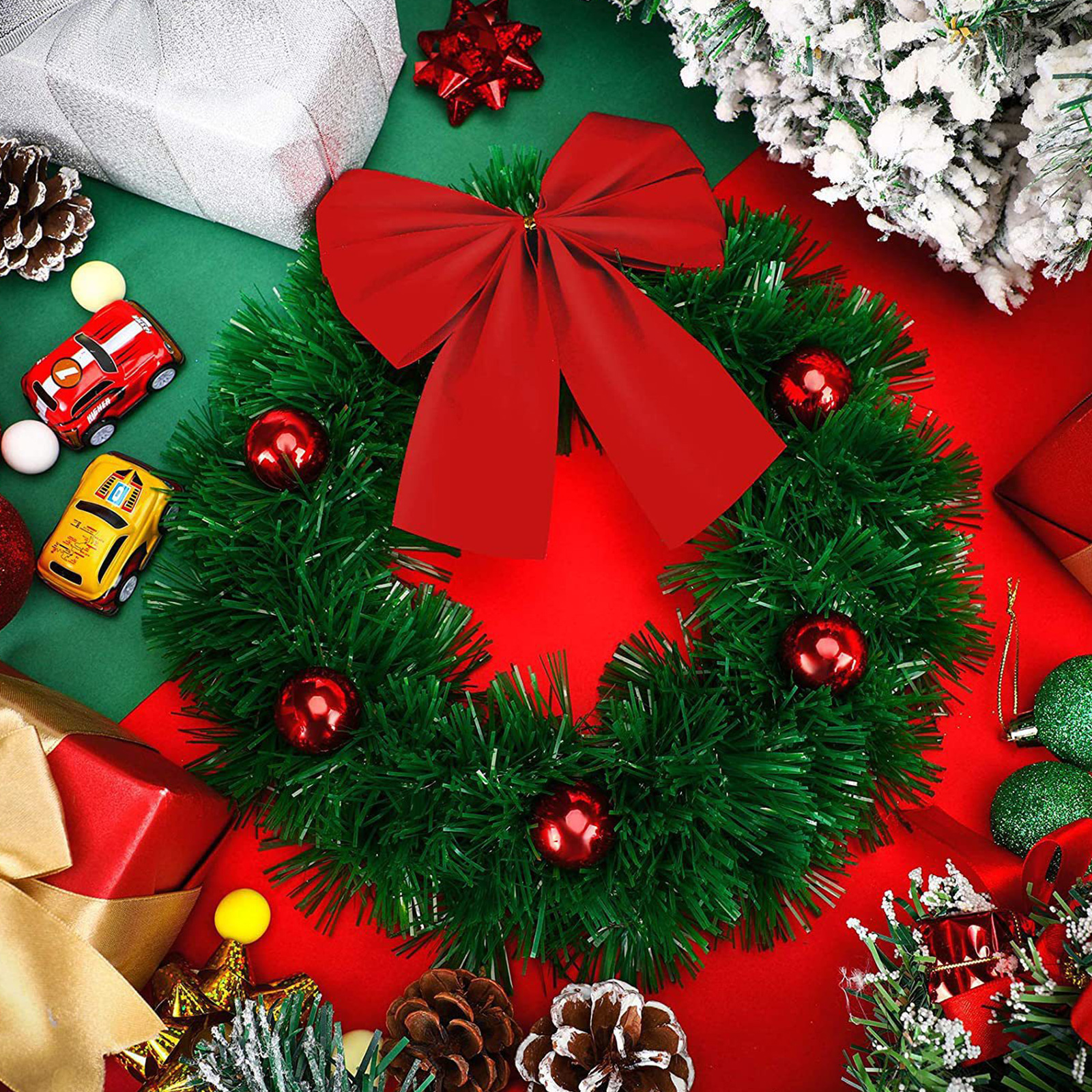 Ein Weihnachtskranz mit roter Schleife und Ornamenten, umgeben von festlichen Dekorationen und Spielzeugautos auf roten und grünen Oberflächen.