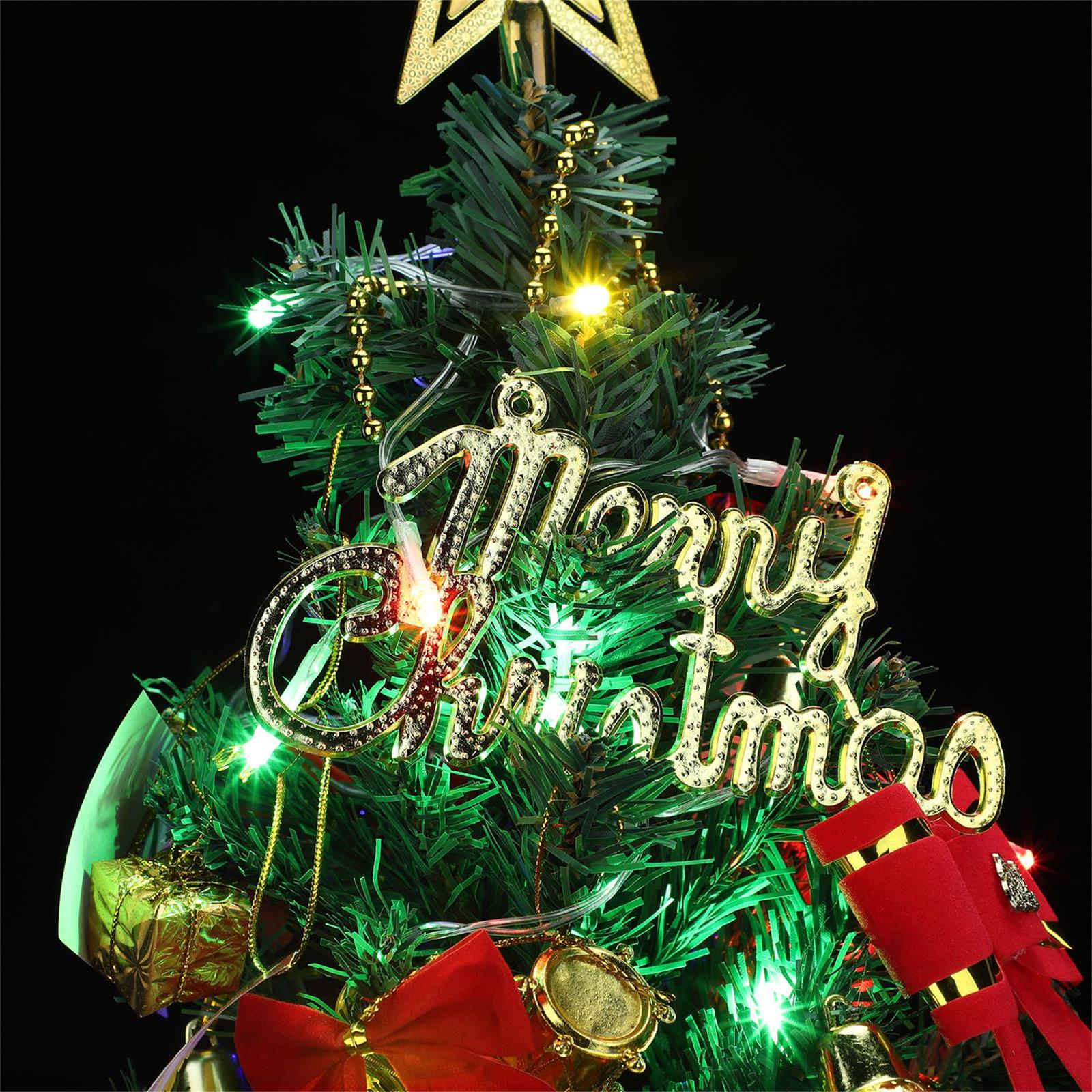 Ein Weihnachtsbaum mit goldenem 'Frohe Weihnachten'-Schild, Ornamenten, Lichtern und einem Stern oben auf schwarzem Grund.