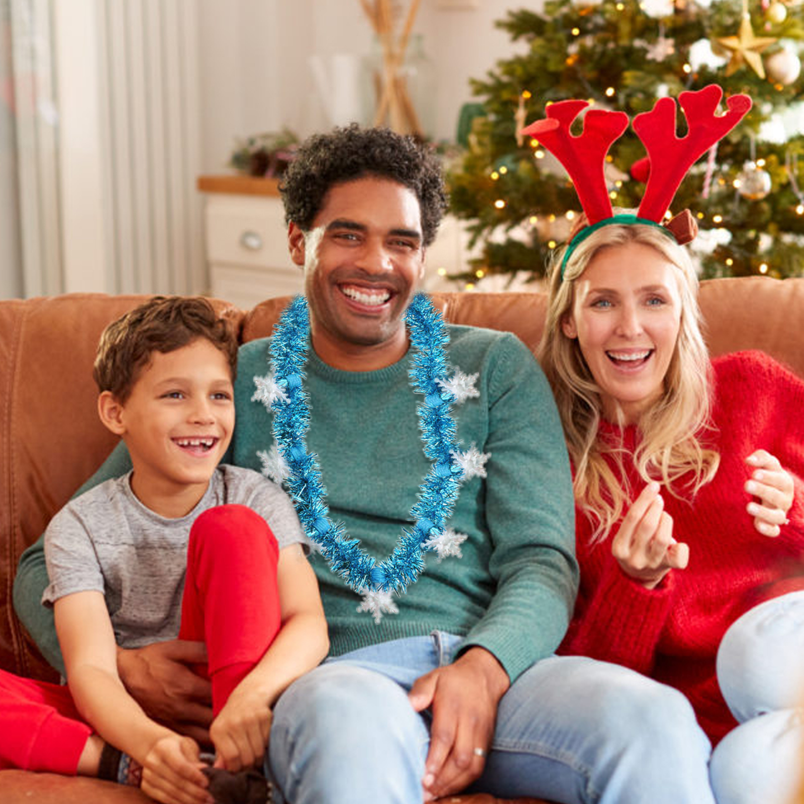 Eine Familie lächelt auf einer Couch vor einem Weihnachtsbaum. Papa trägt eine Girlande. Mama hat Rentiergeweihe.
