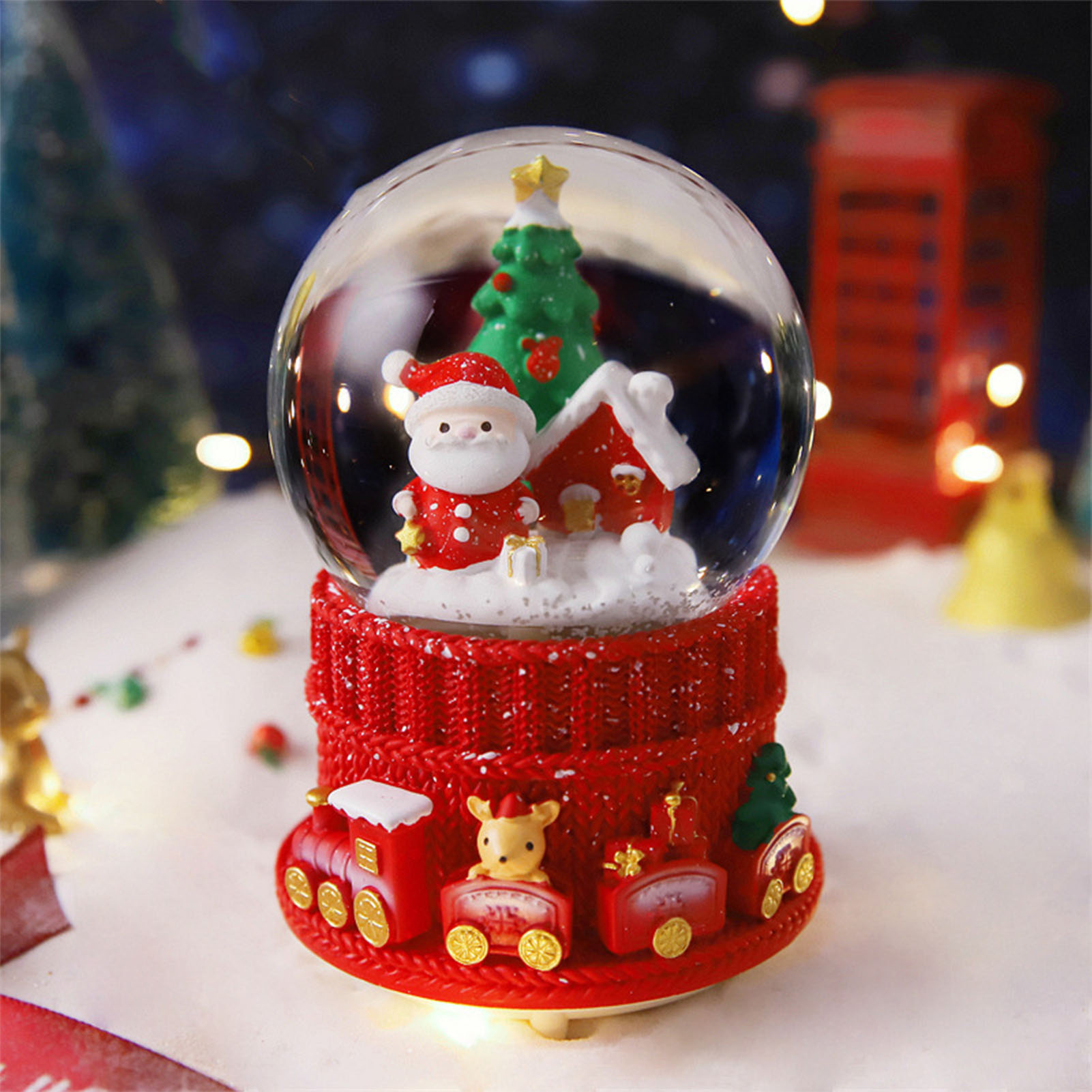 Eine Weihnachtsschneekugel mit Weihnachtsmann, Haus und Baum. Der Sockel ist rot mit einem Zug. Hintergrund hat Bokeh-Lichter.